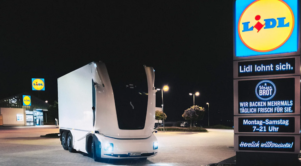 Ein futuristischer, weißer LKW steht nachts auf dem Parkplatz eines Lidl-Supermarkts.