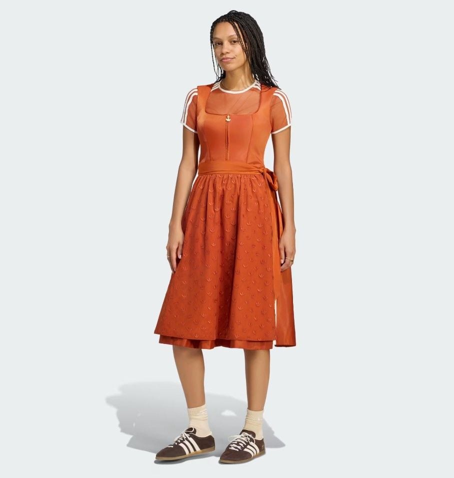 Frau trägt ein orangefarbenes Dirndl mit Adidas-Sneakern und weißen Socken.