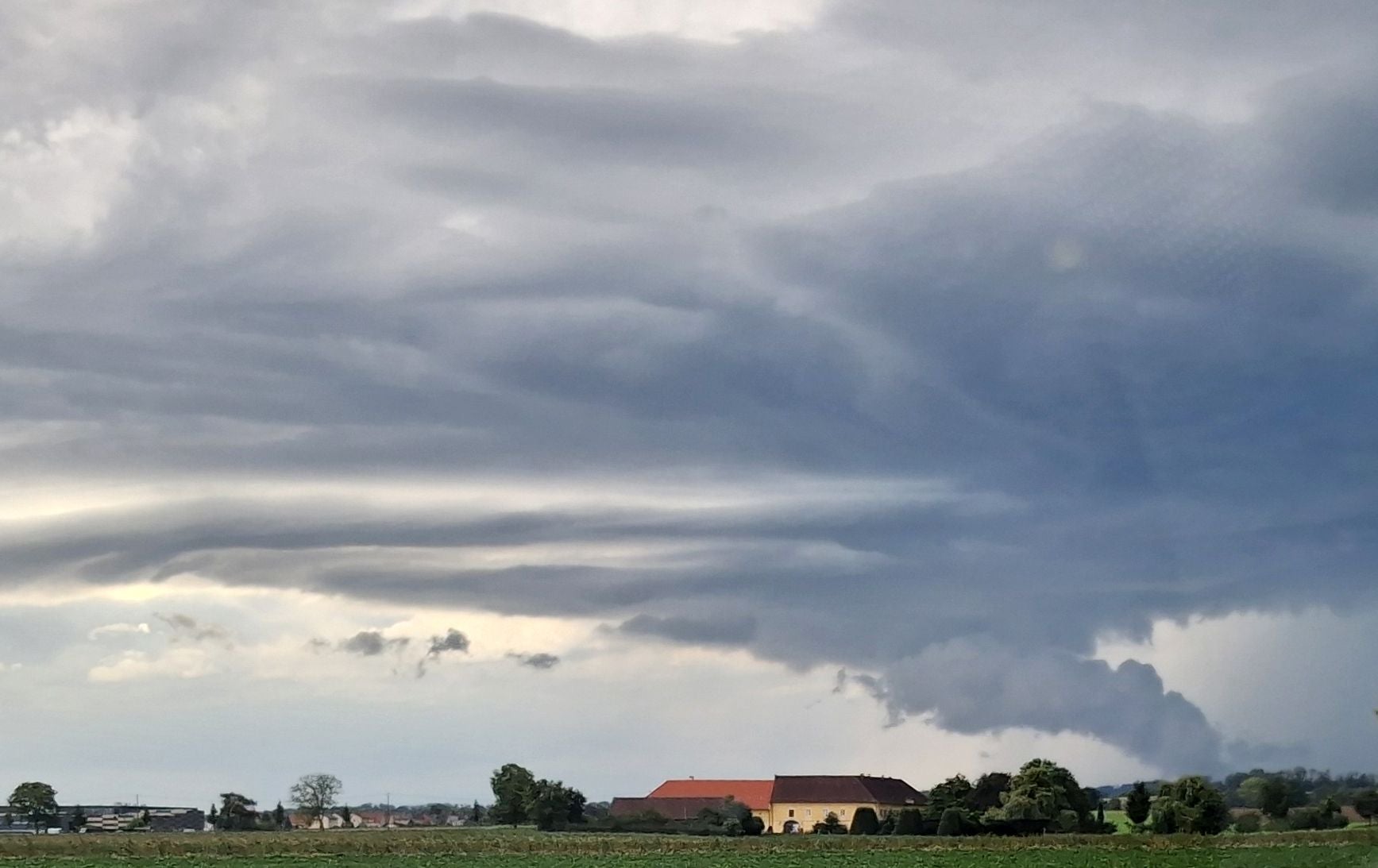 Dunkle Sturmwolken über Feldern und Gebäuden bei Pasching in Oberösterreich.