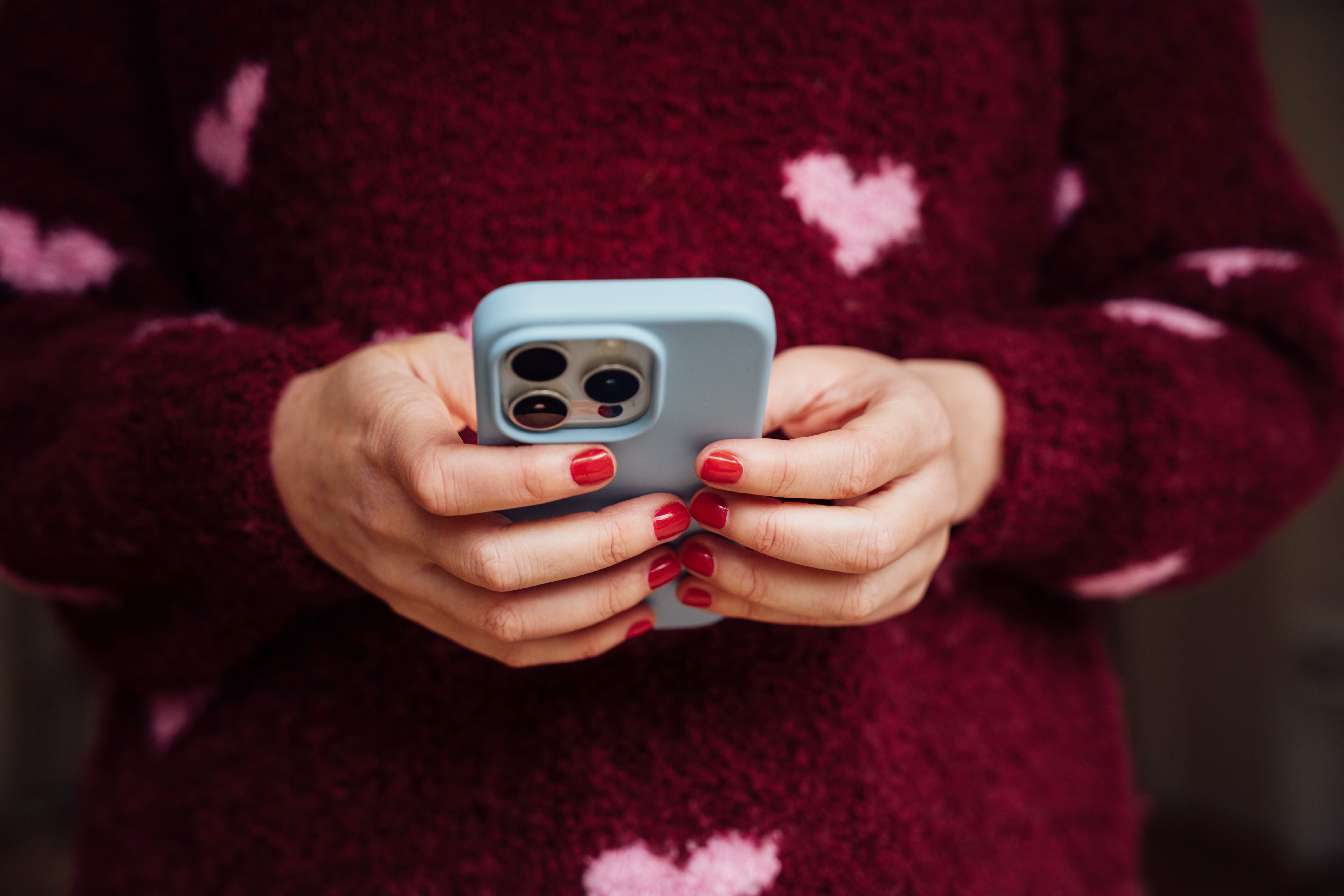 Frau mit rot lackierten Nägeln hält ein Smartphone mit hellblauer Hülle in der Hand.