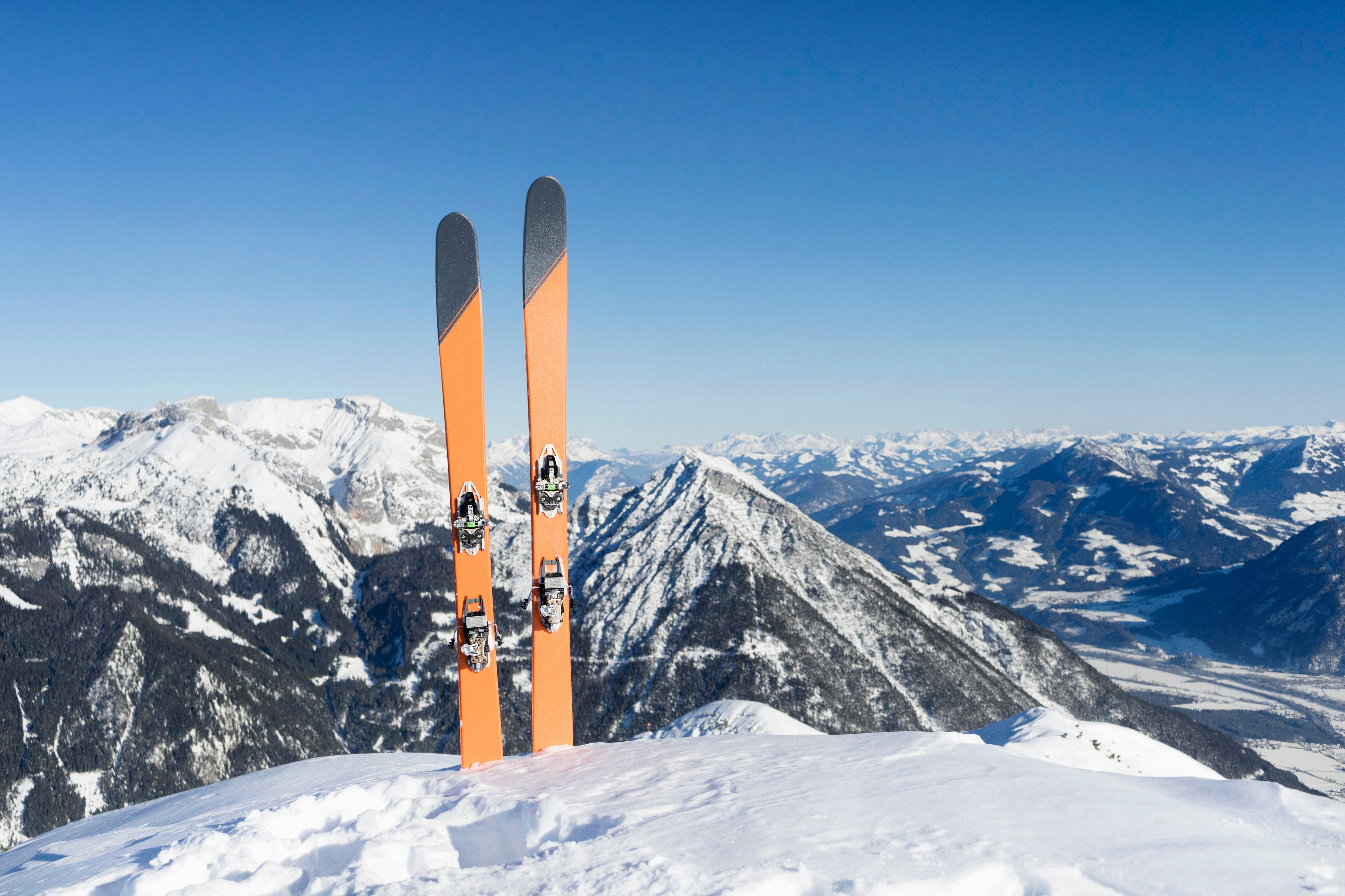 Zwei orange Skier stehen im Schnee vor verschneiten Bergen in Tirol, Österreich.