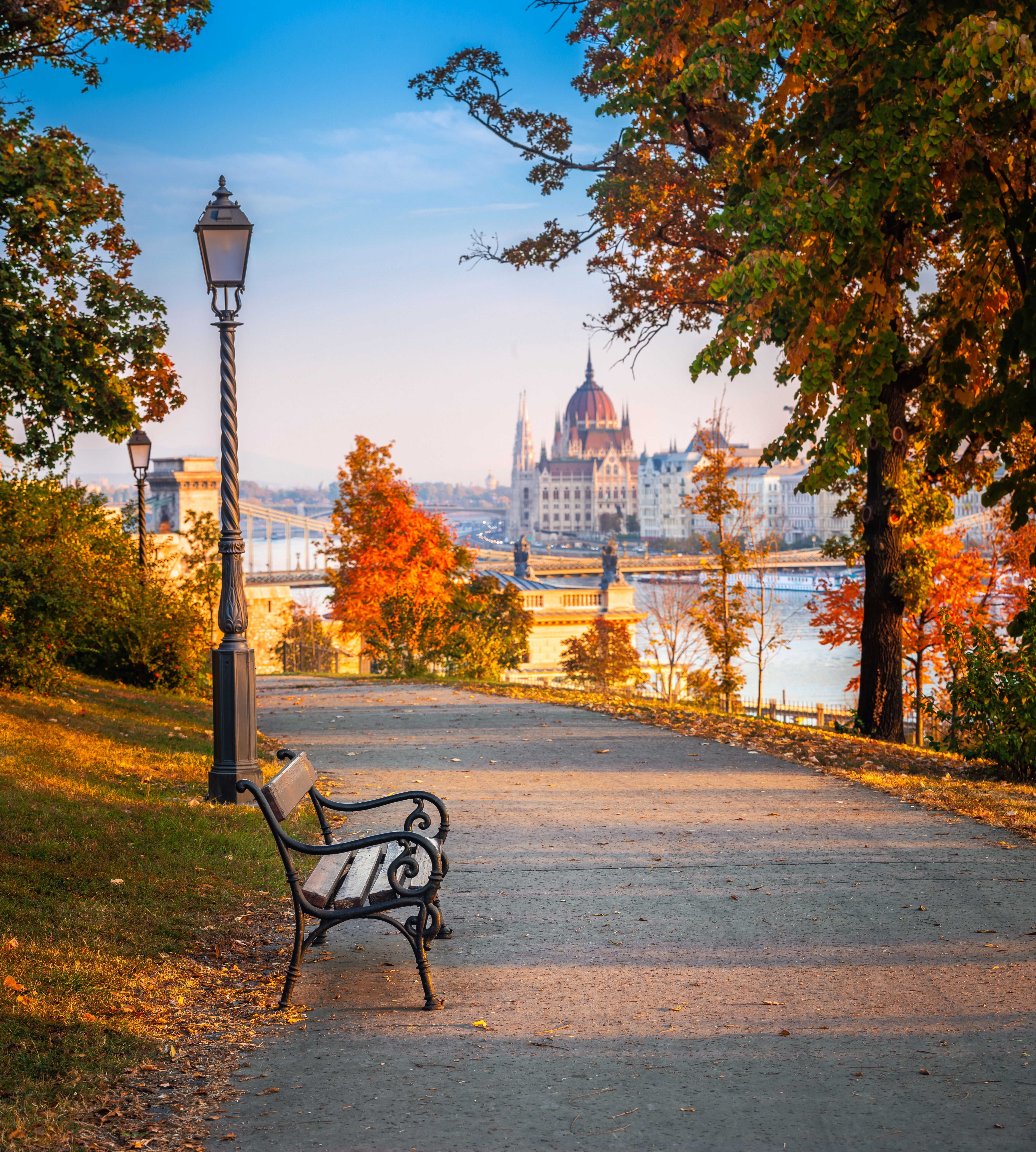 Bank im herbstlichen Park mit Blick auf das Parlament und die Kettenbrücke in Budapest bei Sonnenaufgang.