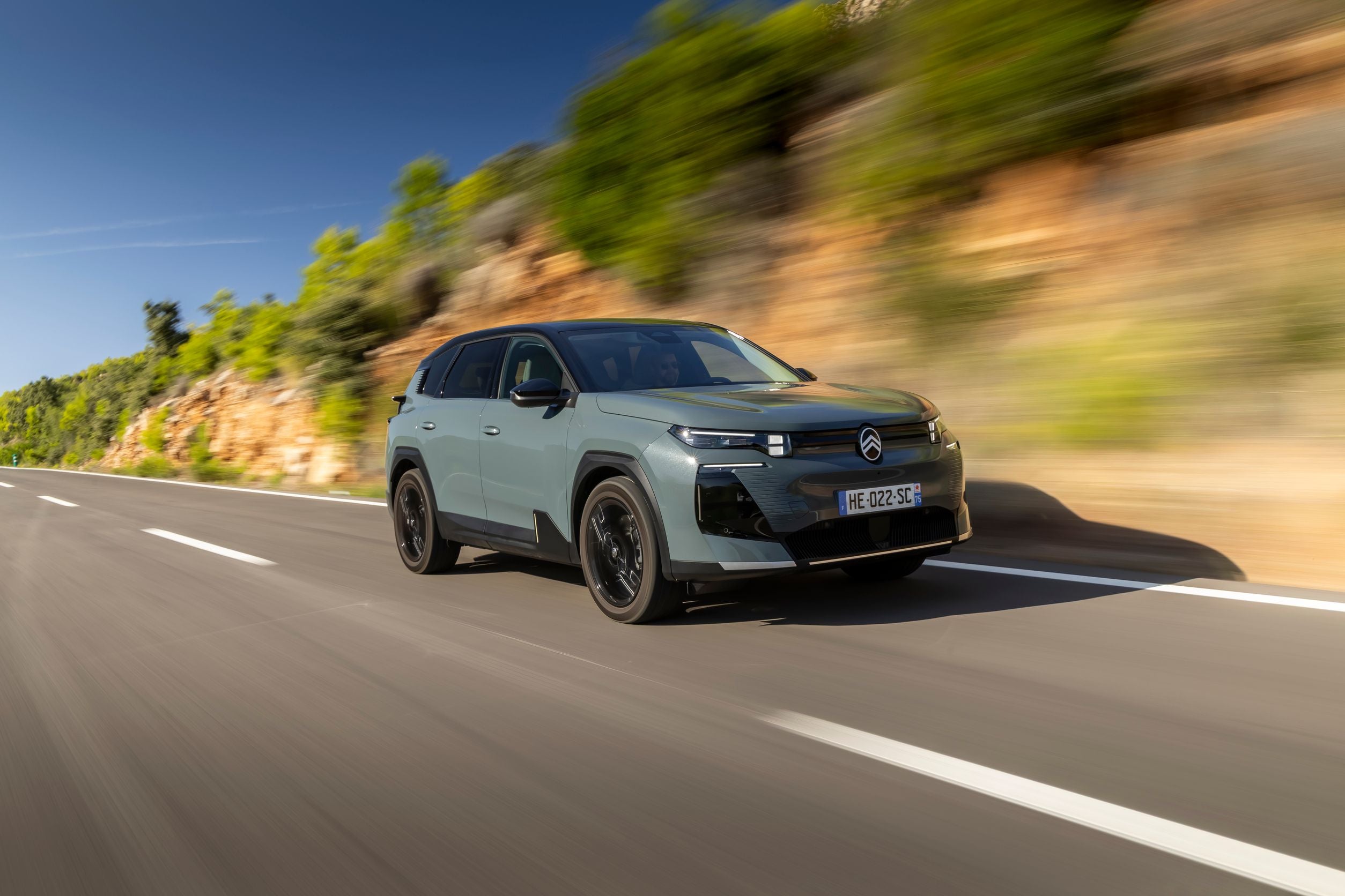 Grauer Citroën-SUV fährt auf einer Landstraße an Felsen und grüner Vegetation vorbei.