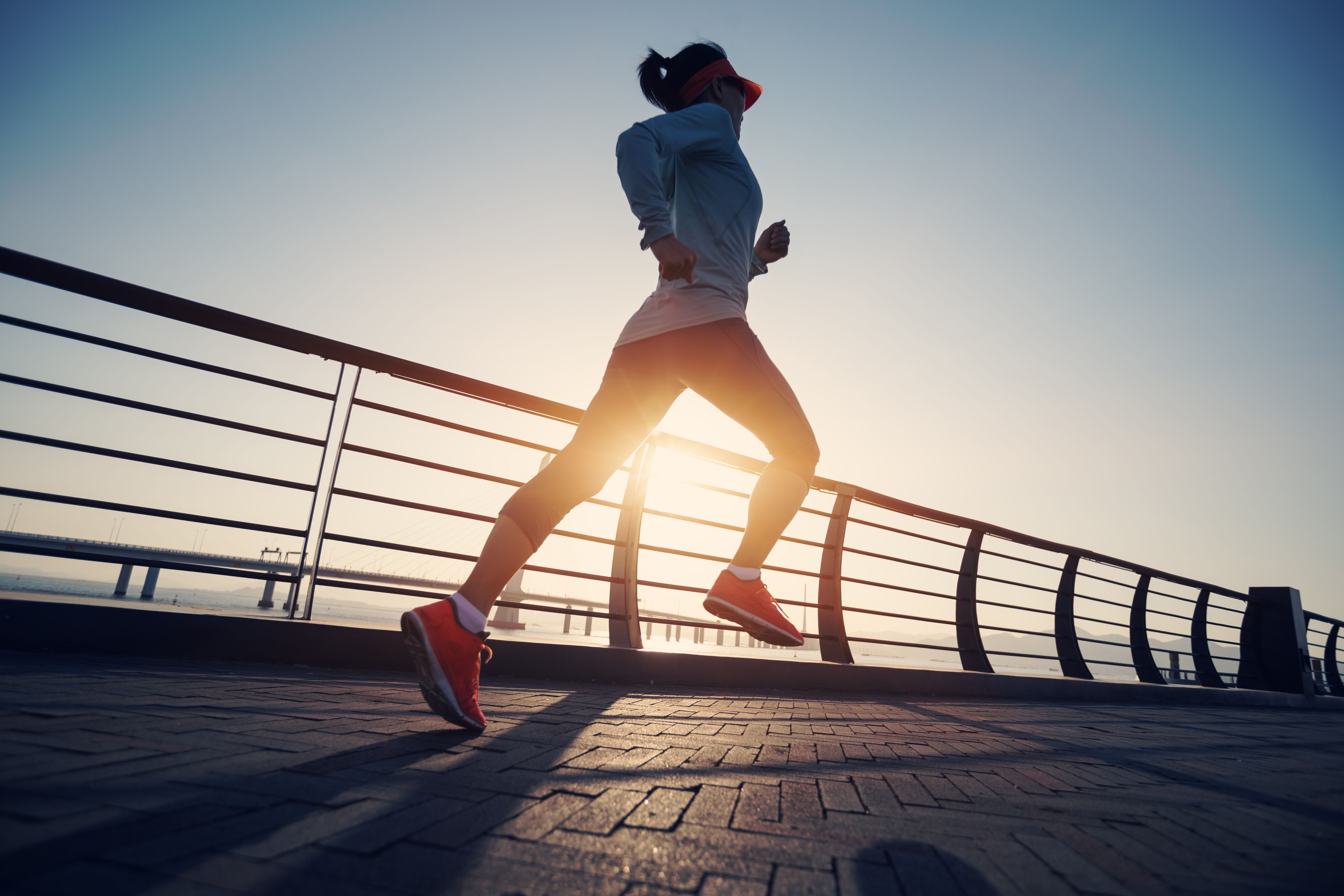Joggerin läuft bei Sonnenaufgang auf einer Brücke am Wasser entlang.