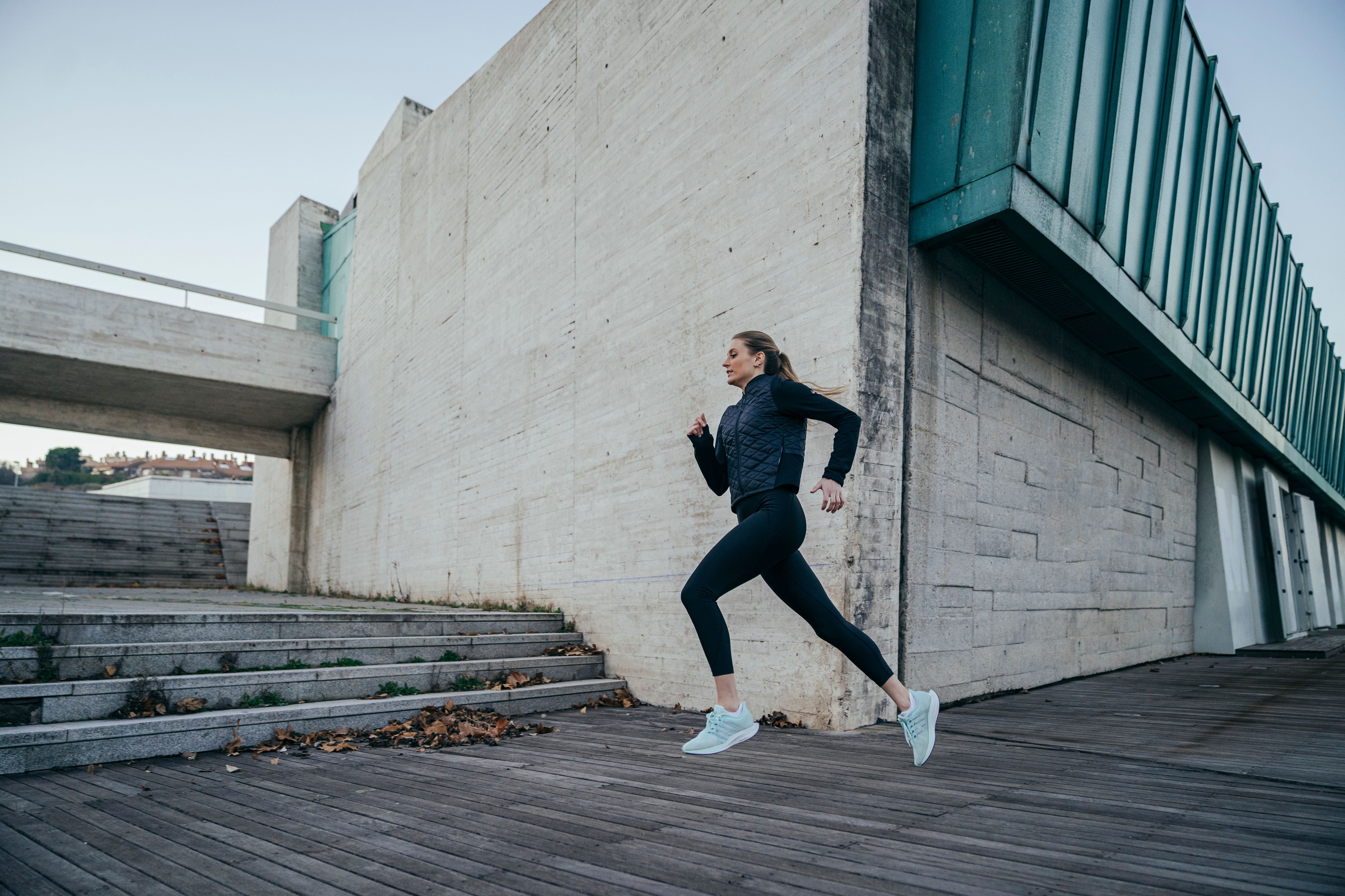 Frau in schwarzer Sportkleidung joggt seitlich an einem modernen Gebäude vorbei.