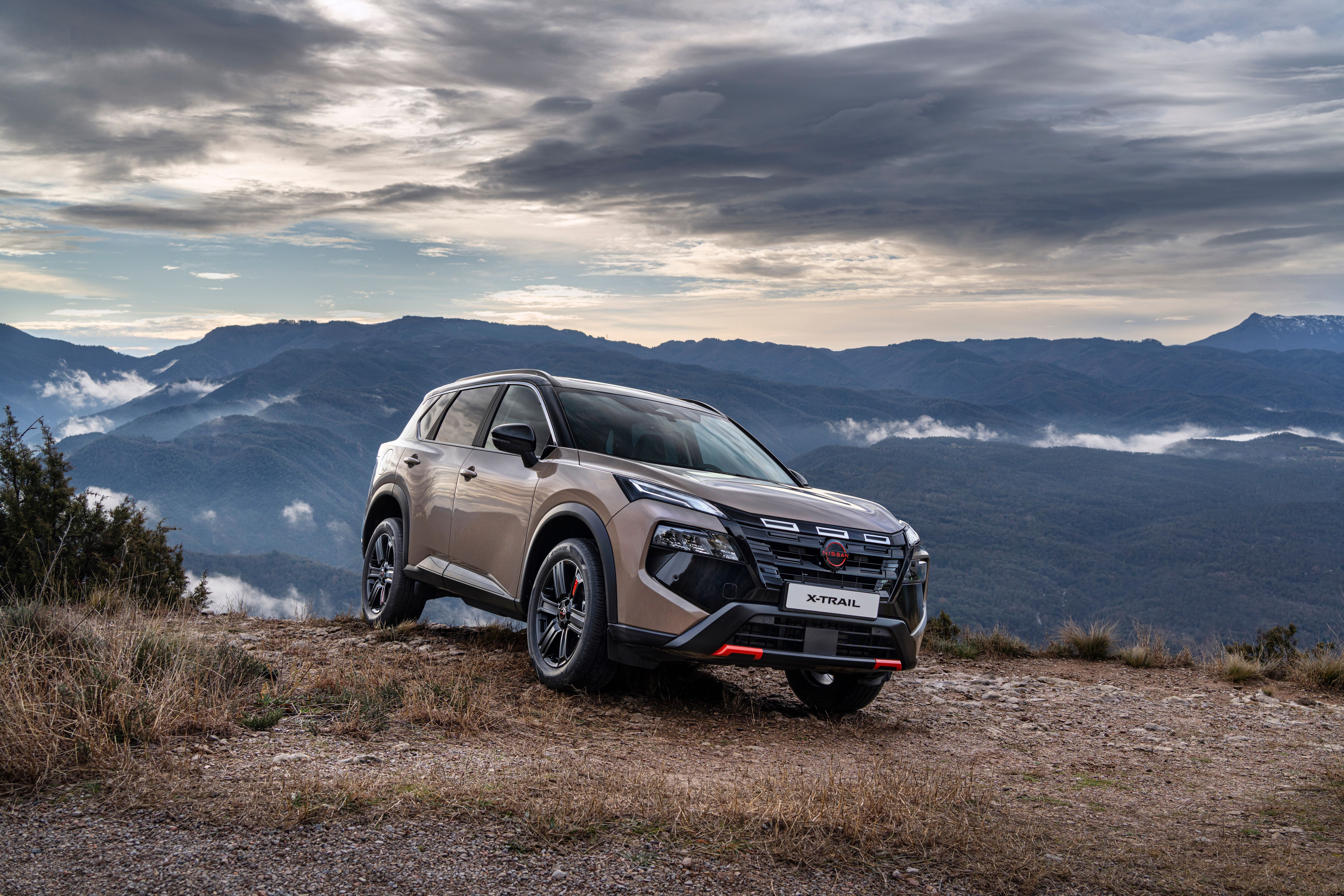 SUV Nissan X-Trail steht auf einem Berg mit Blick auf bewaldete Berge und bewölkten Himmel.