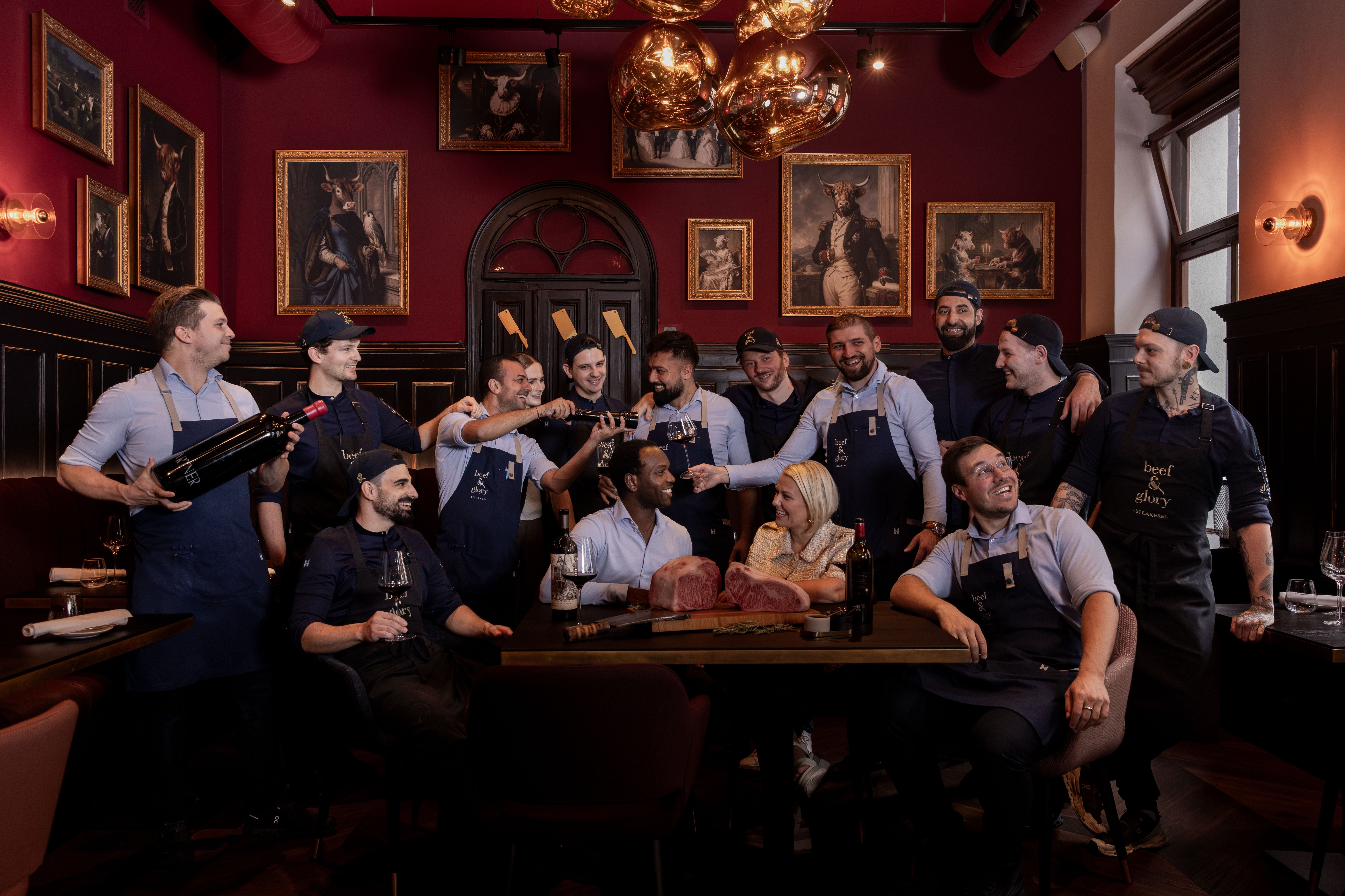 Gruppenfoto eines Restaurantteams mit Fleisch und Wein im stilvoll dekorierten Raum bei beef & glory.