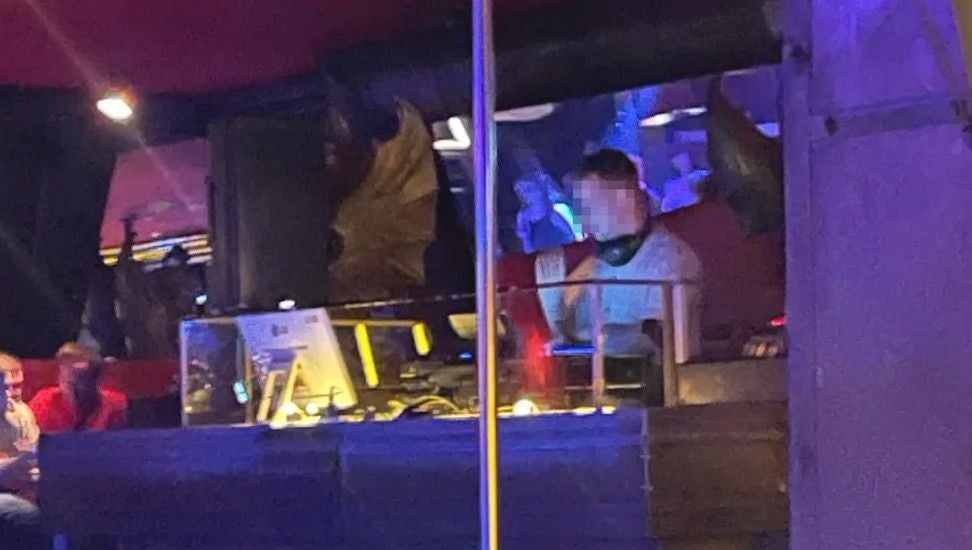 Ein DJ legt in einem Club auf, sein Gesicht ist verpixelt, buntes Licht im Hintergrund.