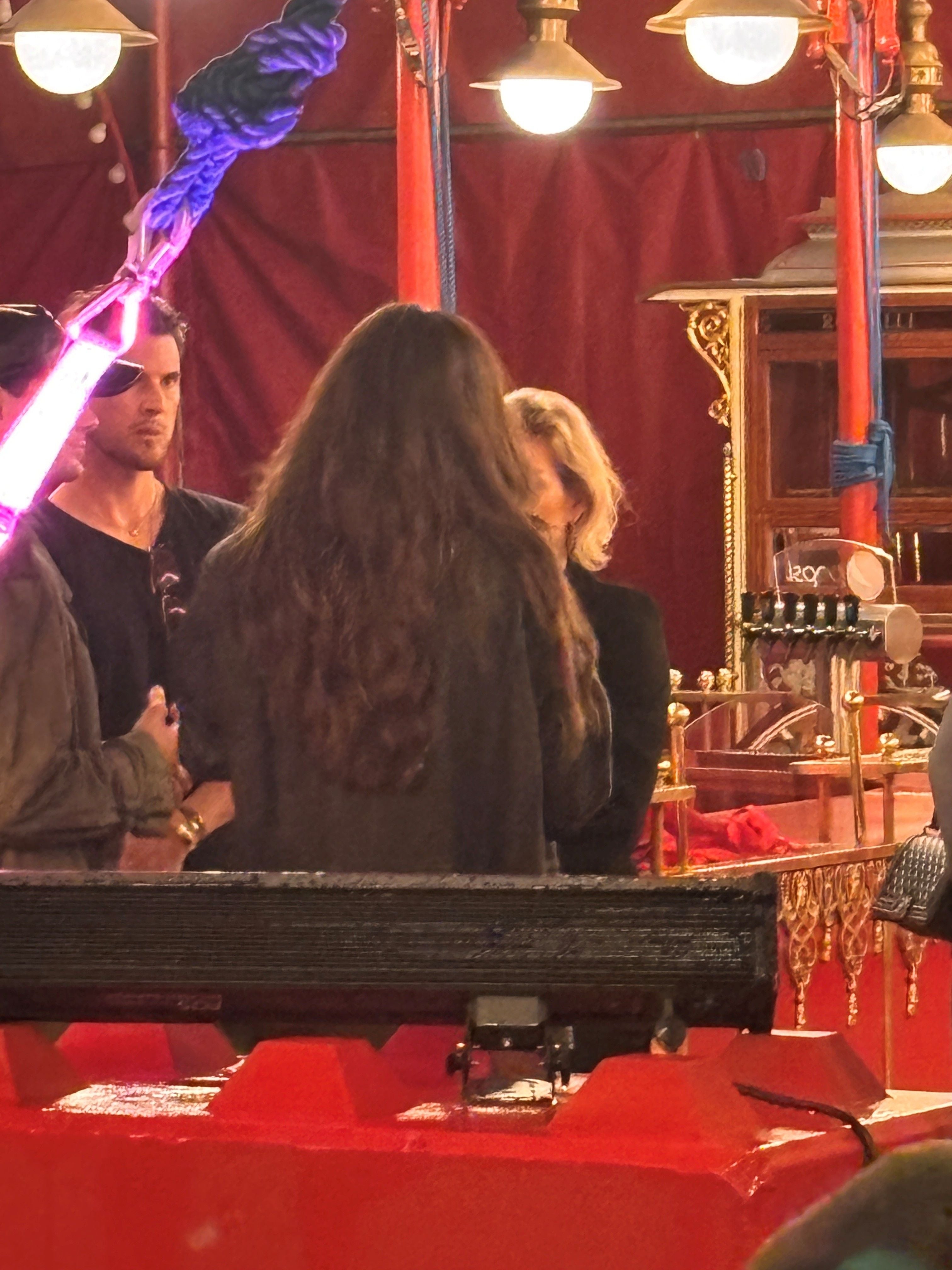 Mehrere Personen stehen angespannt in einem festlich beleuchteten Zelt mit rotem Dekor.