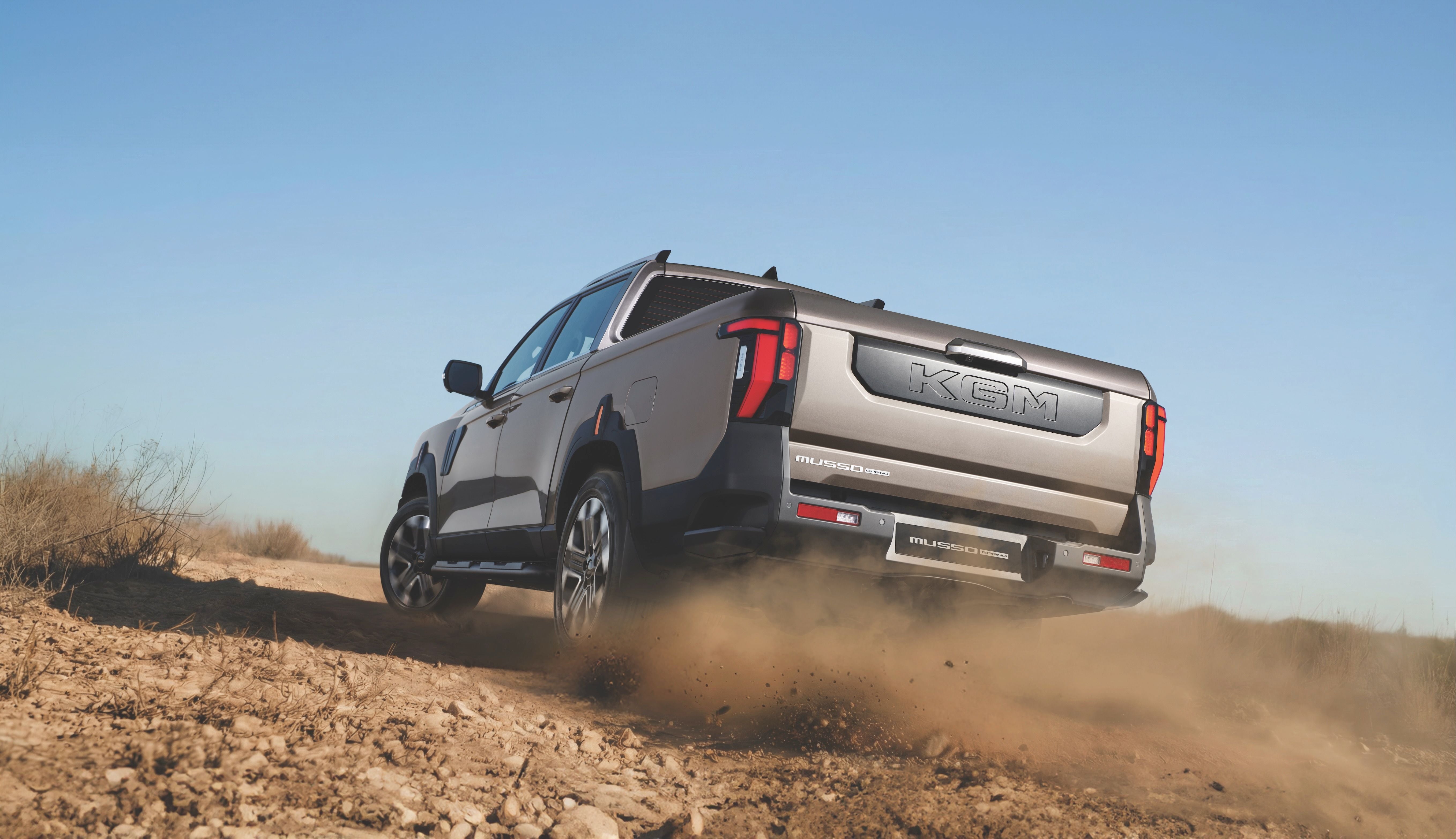 Ein silberner Pickup fährt auf einer staubigen Offroad-Strecke durch trockene Landschaft.