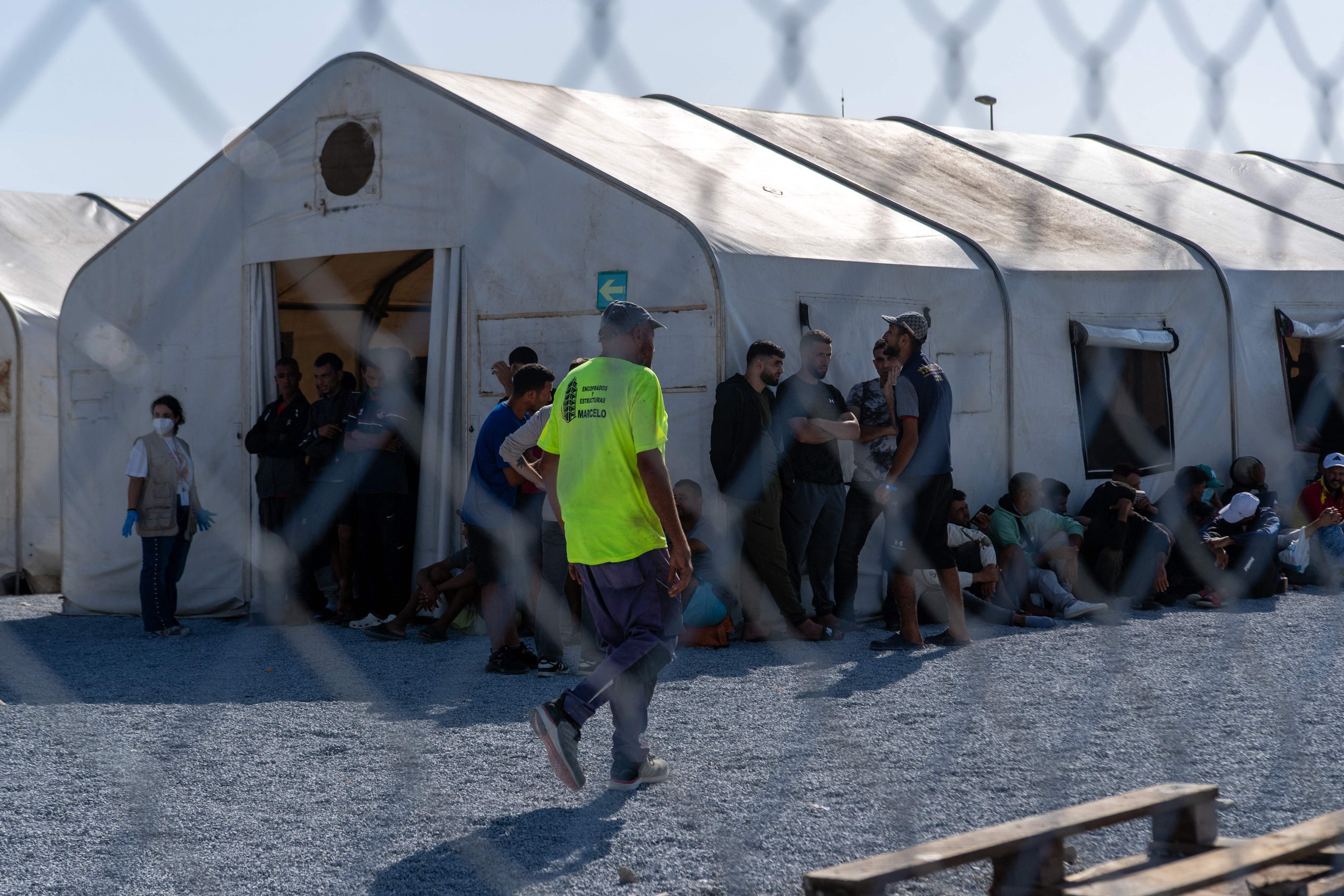 Menschen sitzen und stehen vor großen Zelten in einem überfüllten Migrantenaufnahmelager.