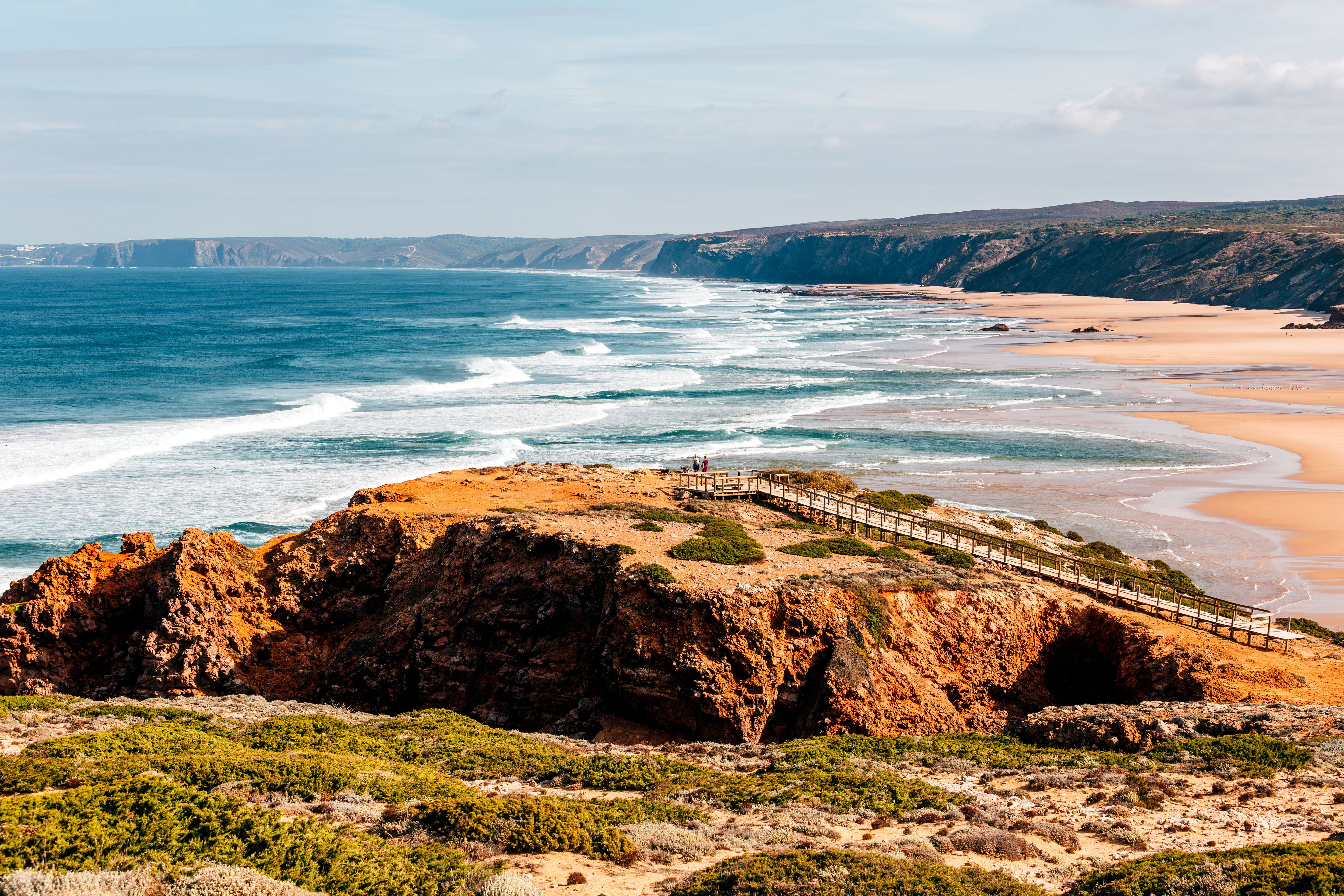 Klippenlandschaft mit Holzsteg und weitem Sandstrand an der Algarve, Portugal.