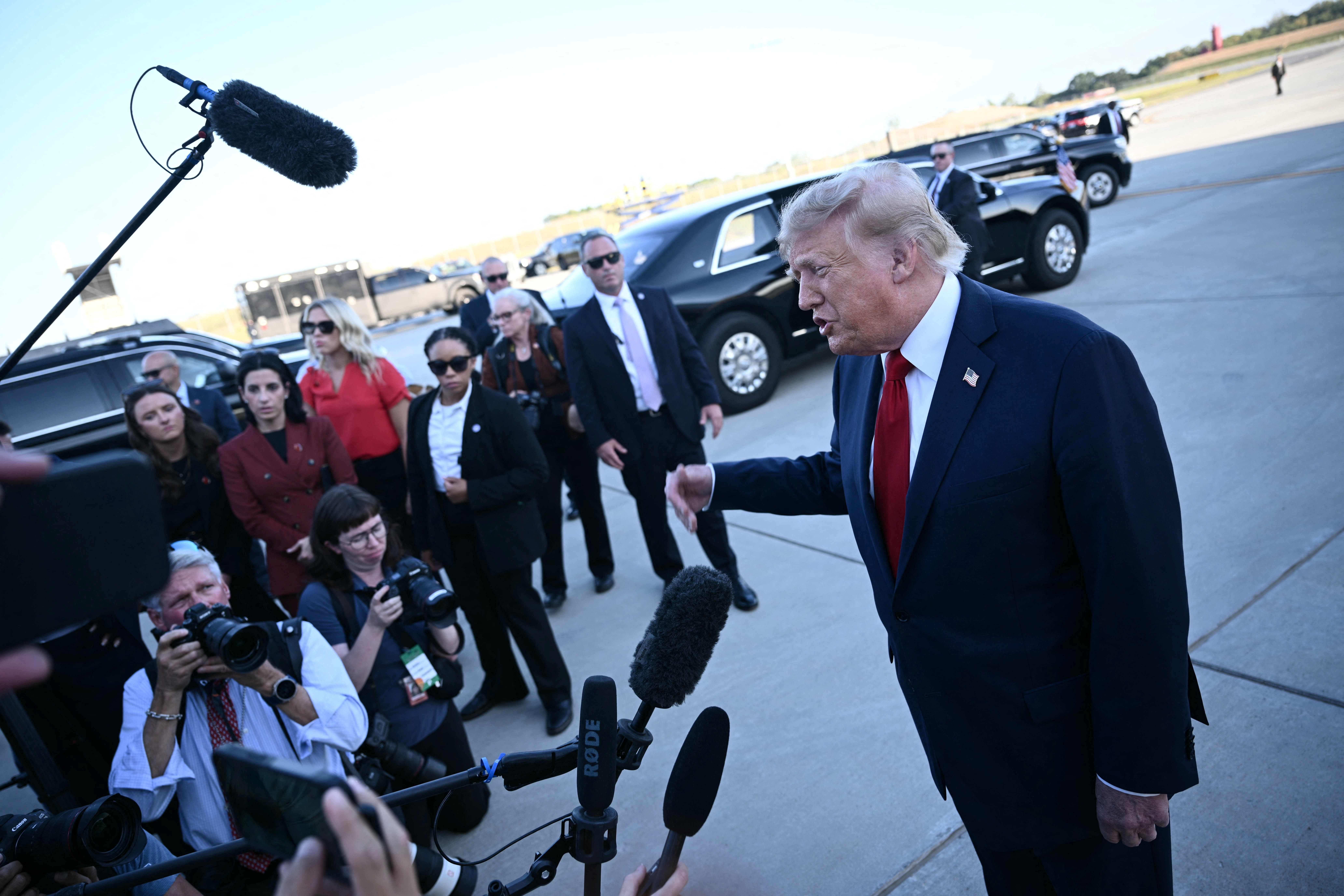 Donald Trump spricht bei einer Pressekonferenz auf einem Flughafen zu Reportern und Fotografen.