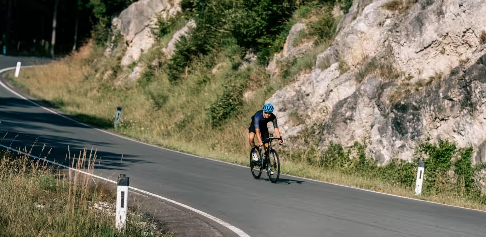 Ein Radfahrer mit blauem Helm fährt auf einer kurvigen Straße an Felsen entlang.