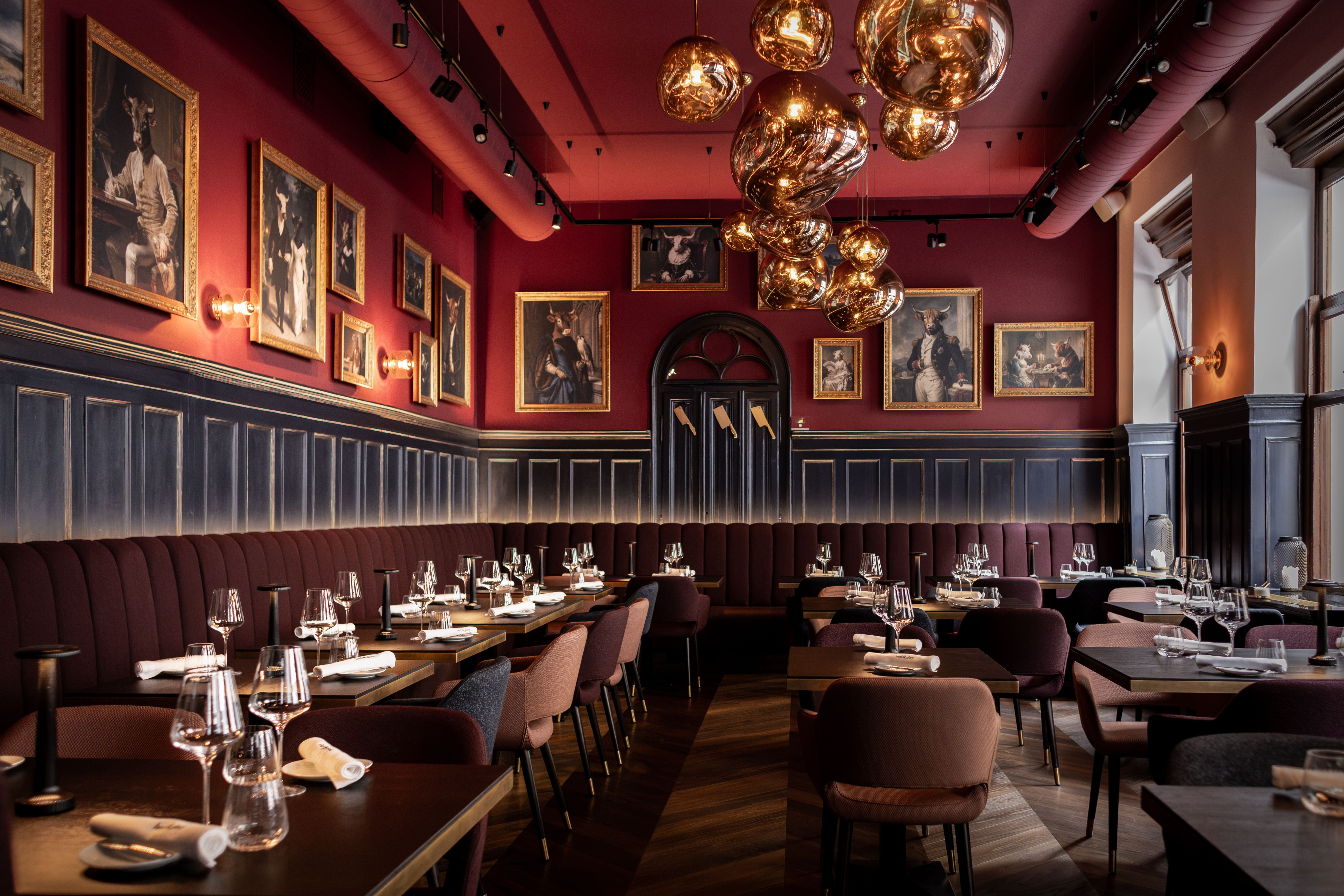 Modernes Restaurant mit roten Wänden, edlen Leuchten und Gemälden, die Tiere in Kleidung zeigen.