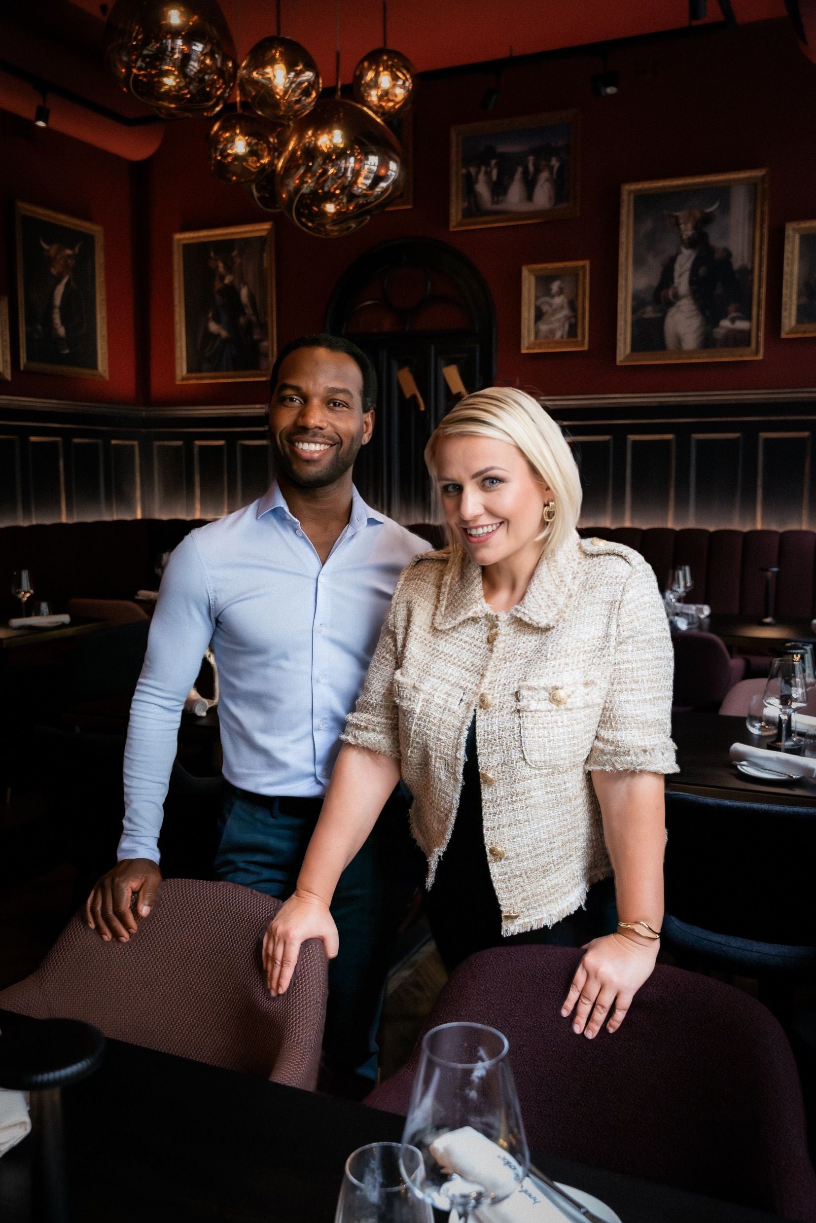 Ein Mann und eine Frau stehen lächelnd in einem stilvoll eingerichteten Restaurant.
