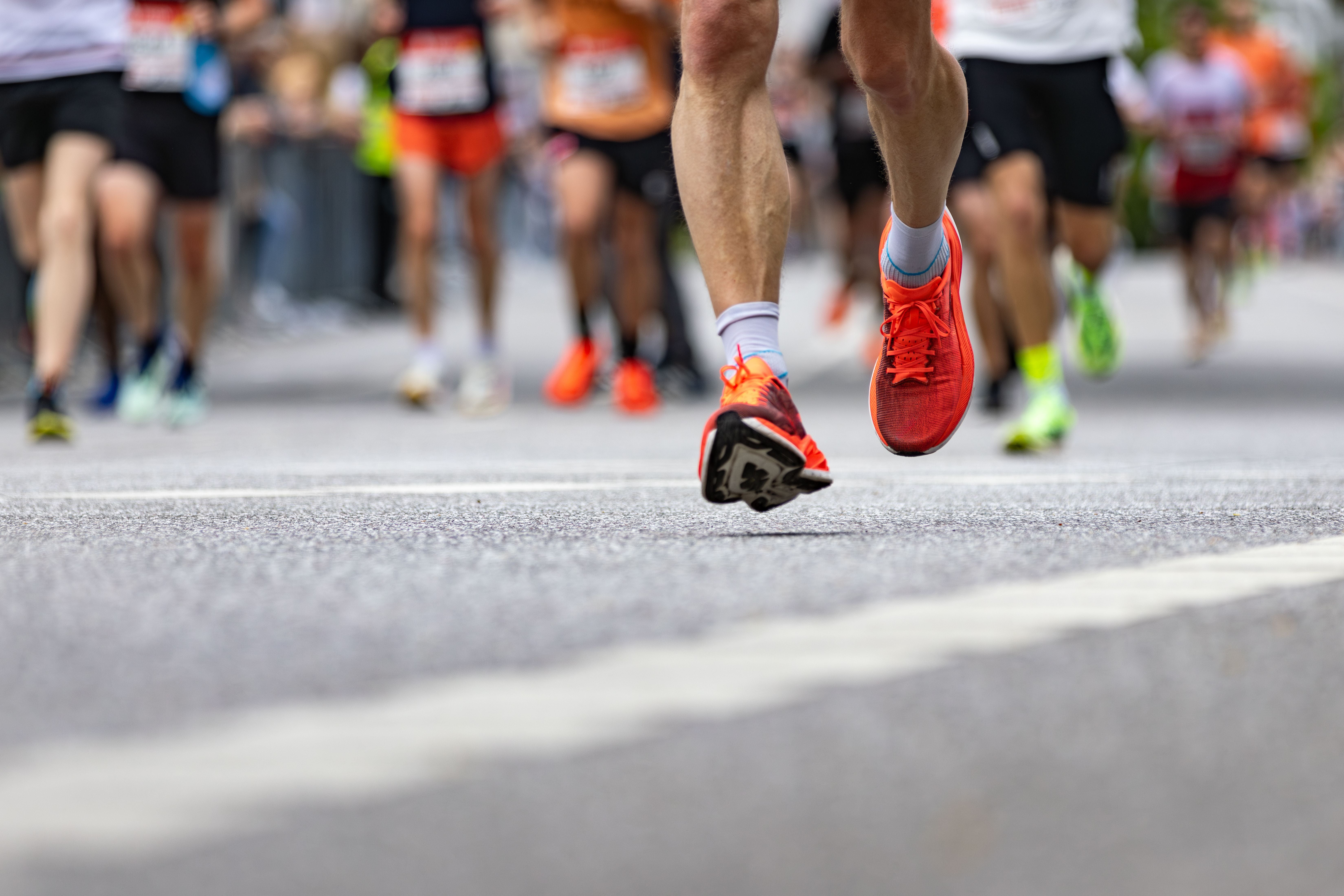 Läufer mit roten Schuhen läuft bei einem Marathon, andere Läufer im Hintergrund.
