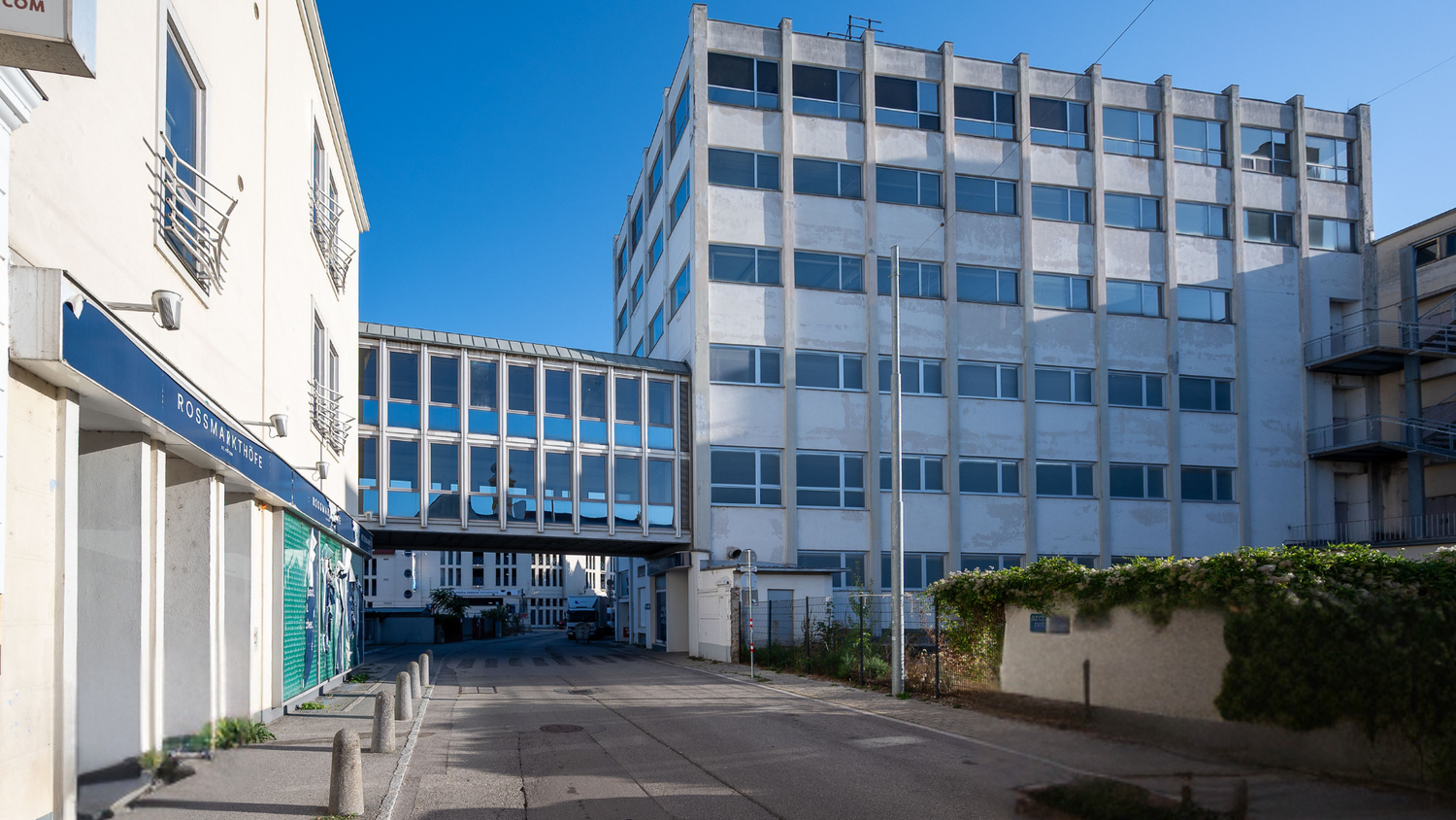 Bürogebäude mit Glasbrücke über einer Straße, links ein Geschäft mit blauem Schild "Rossmarkthöfe".