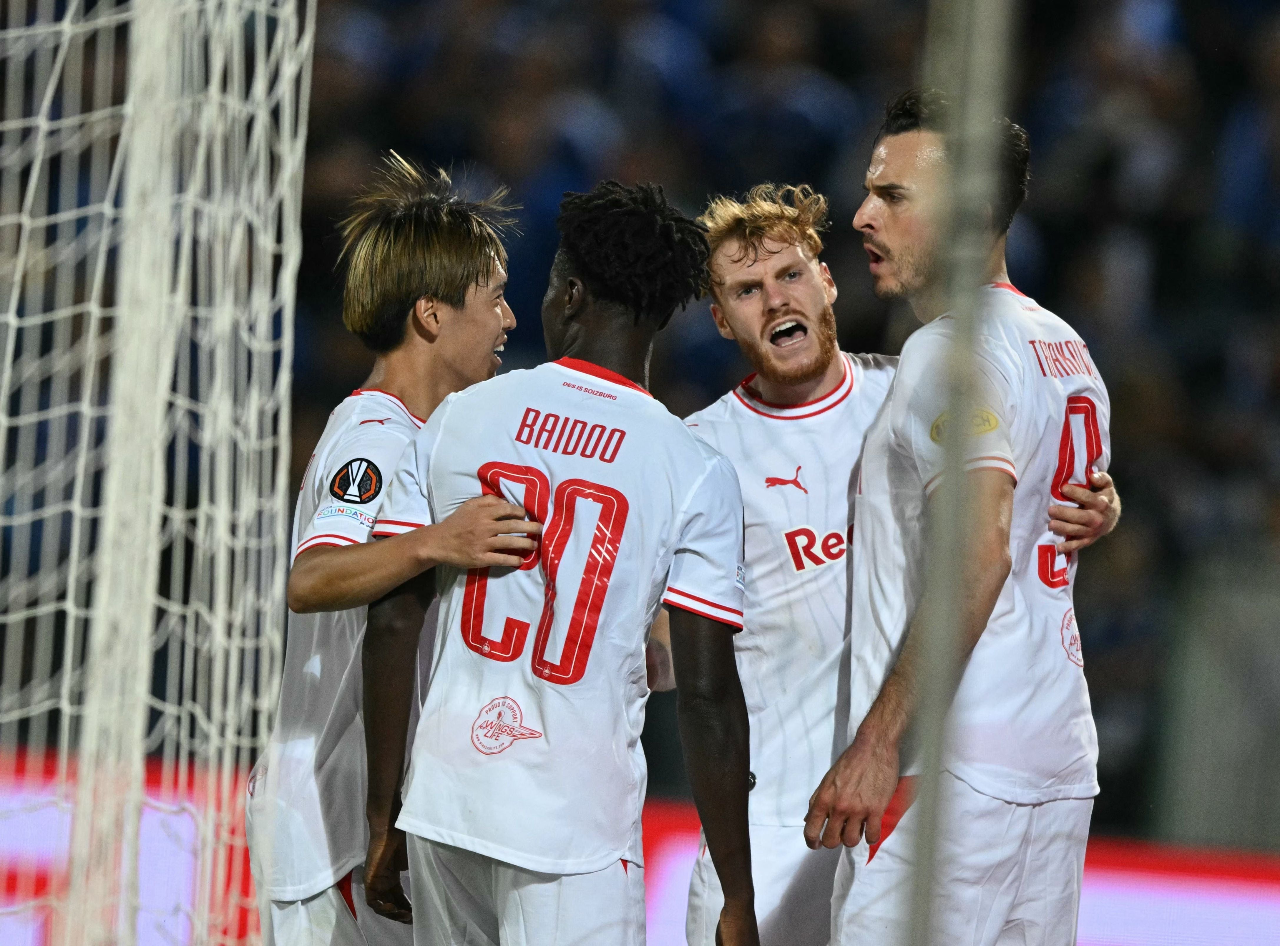 Die Salzburger Kicker Sota Kitano, Samson Baidoo, Bartosz Mazurek und Haris Tabakovic bejubeln im weißen Auswärtstrikot gemeinsam den Führungstreffer nahe des Tornetzes.