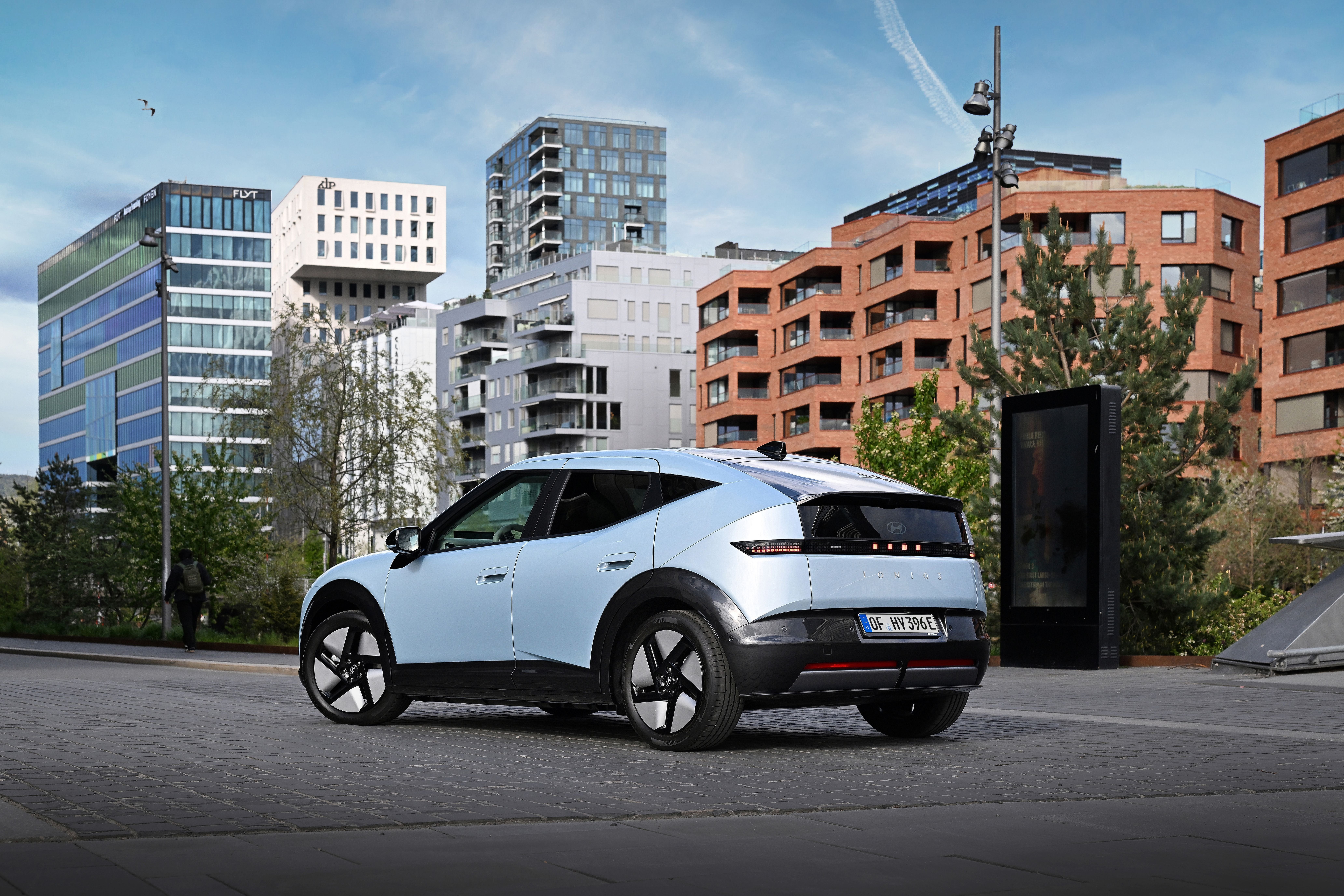 Silbernes Elektroauto steht auf einer Straße vor modernen Wohn- und Bürogebäuden.