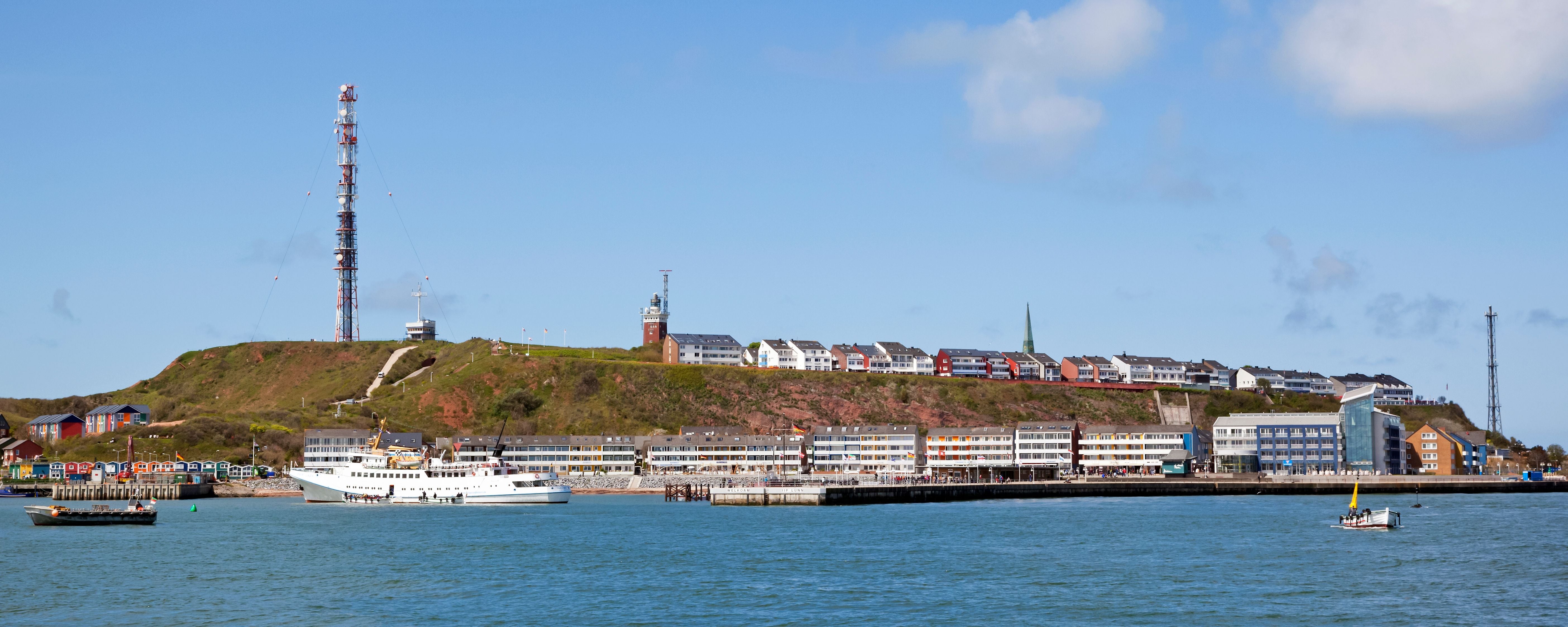 Aussicht auf Helgoland mit bunten Häusern, Hafen, Hotels und einem Sendemast am Meer.