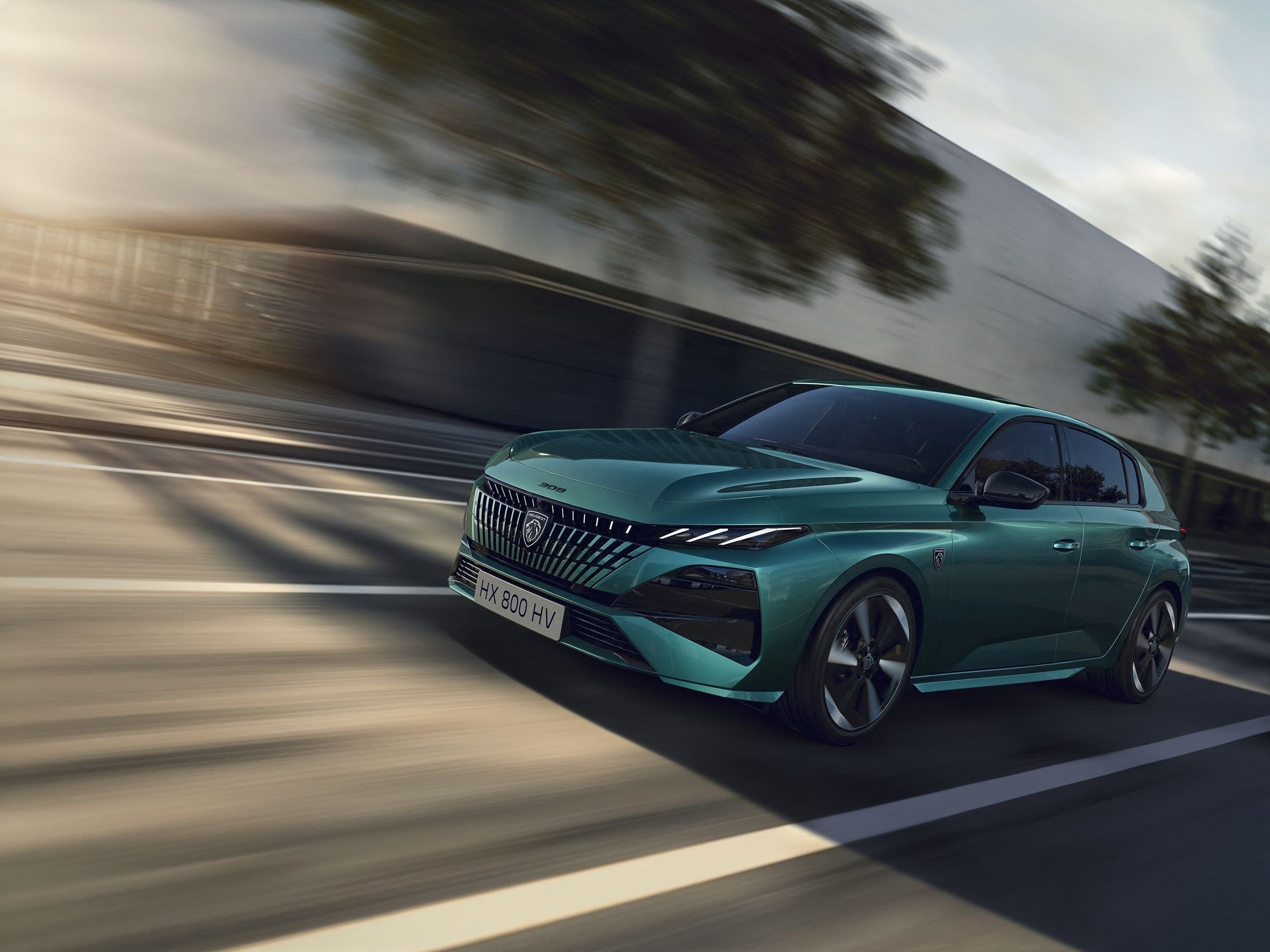 Grüner Peugeot fährt schnell auf einer Straße mit verschwommenem Hintergrund.