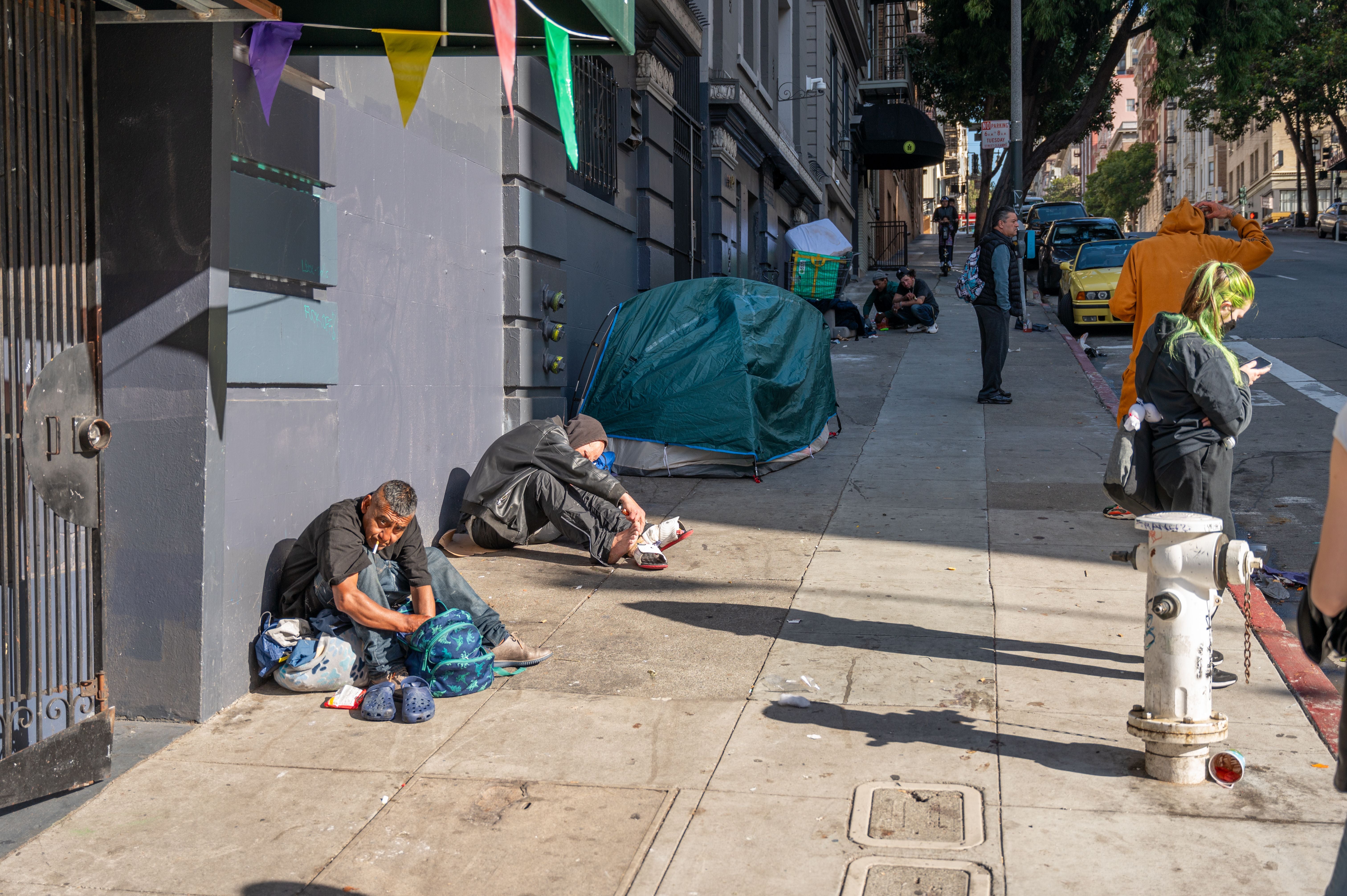 Zwei obdachlose Männer sitzen tagsüber auf dem Gehweg in San Francisco neben einem Zelt.