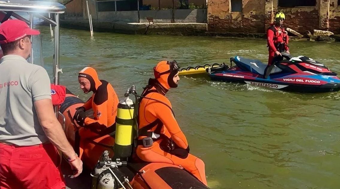 Rettungskräfte in orange Neoprenanzügen und ein Jet-Ski auf einem Kanal in Venedig.