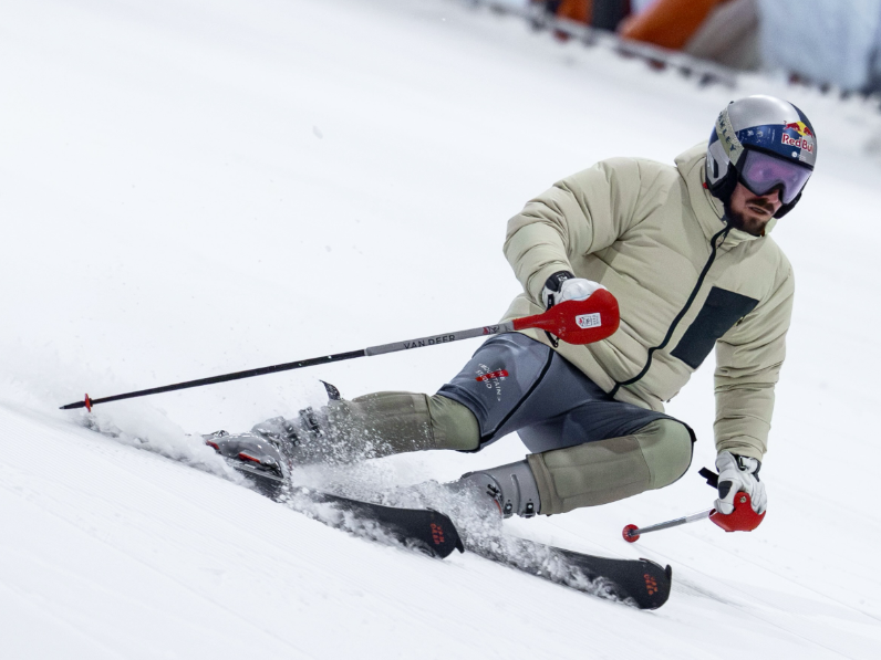Skifahrer mit Helm und Skibrille fährt rasant eine verschneite Piste hinab.