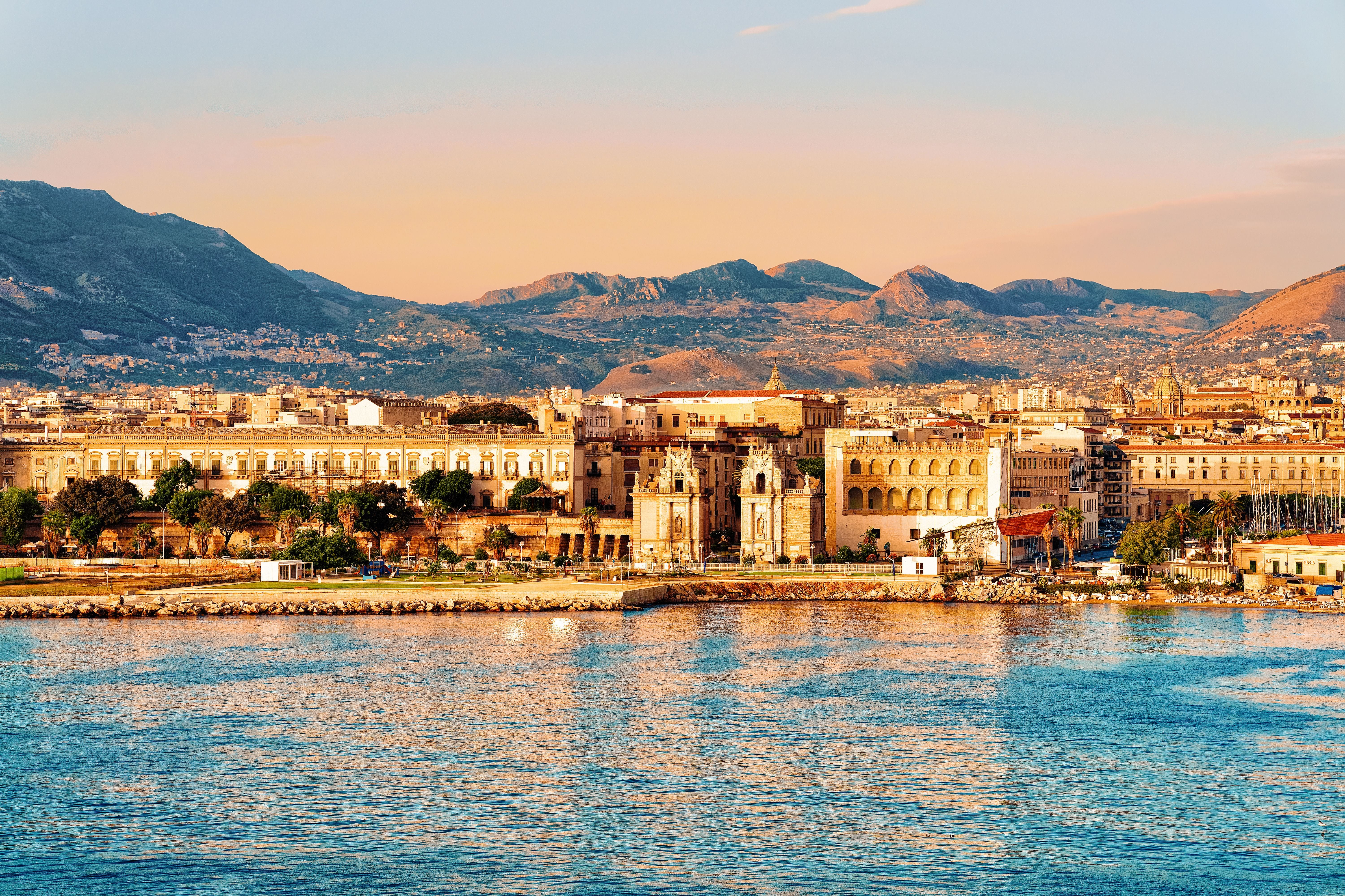 Sonnenaufgang über dem Meer und der Altstadt von Palermo mit Bergen im Hintergrund.