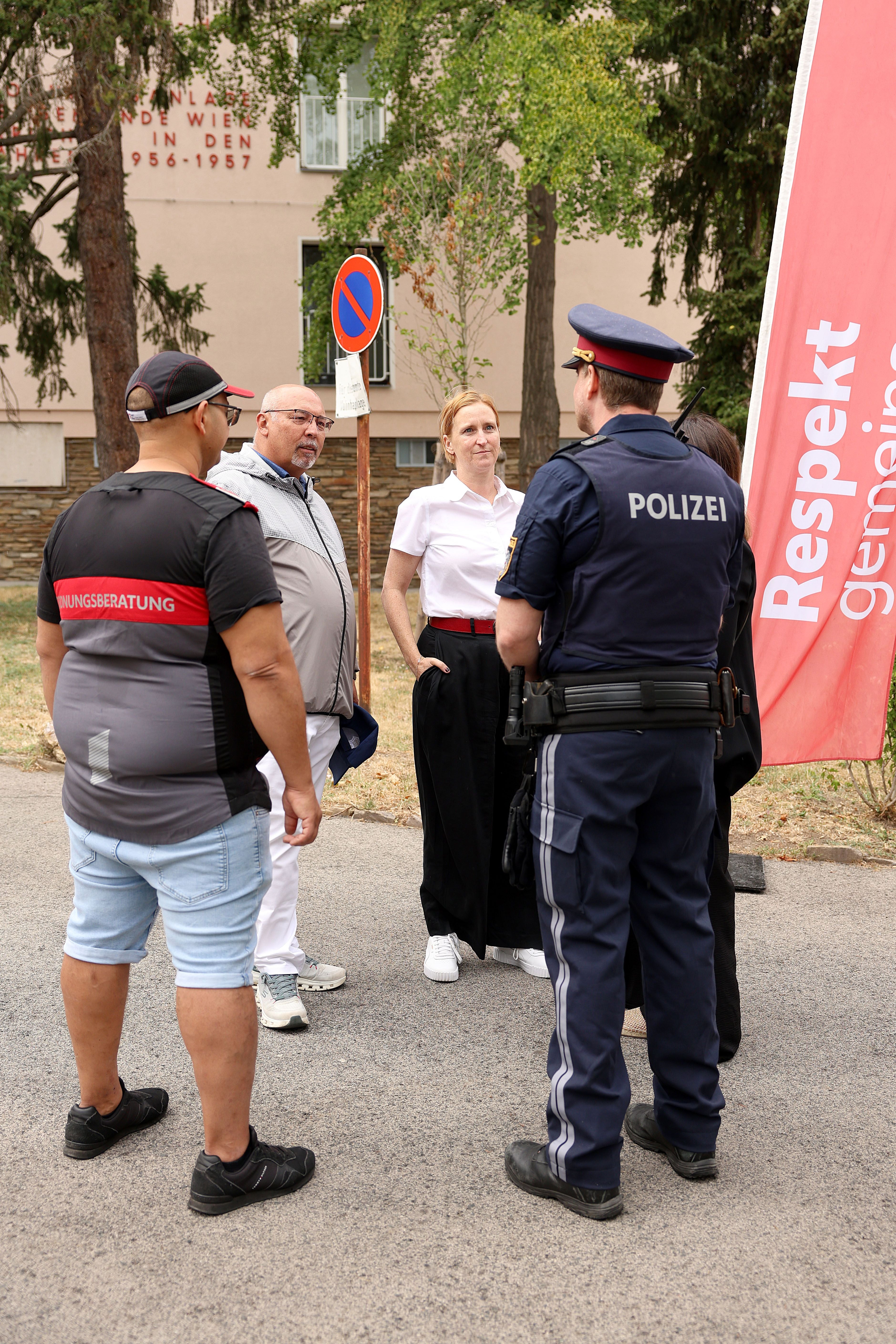 Mehrere Personen, darunter eine Polizistin, stehen im Gespräch bei einem Info-Event im Freien.