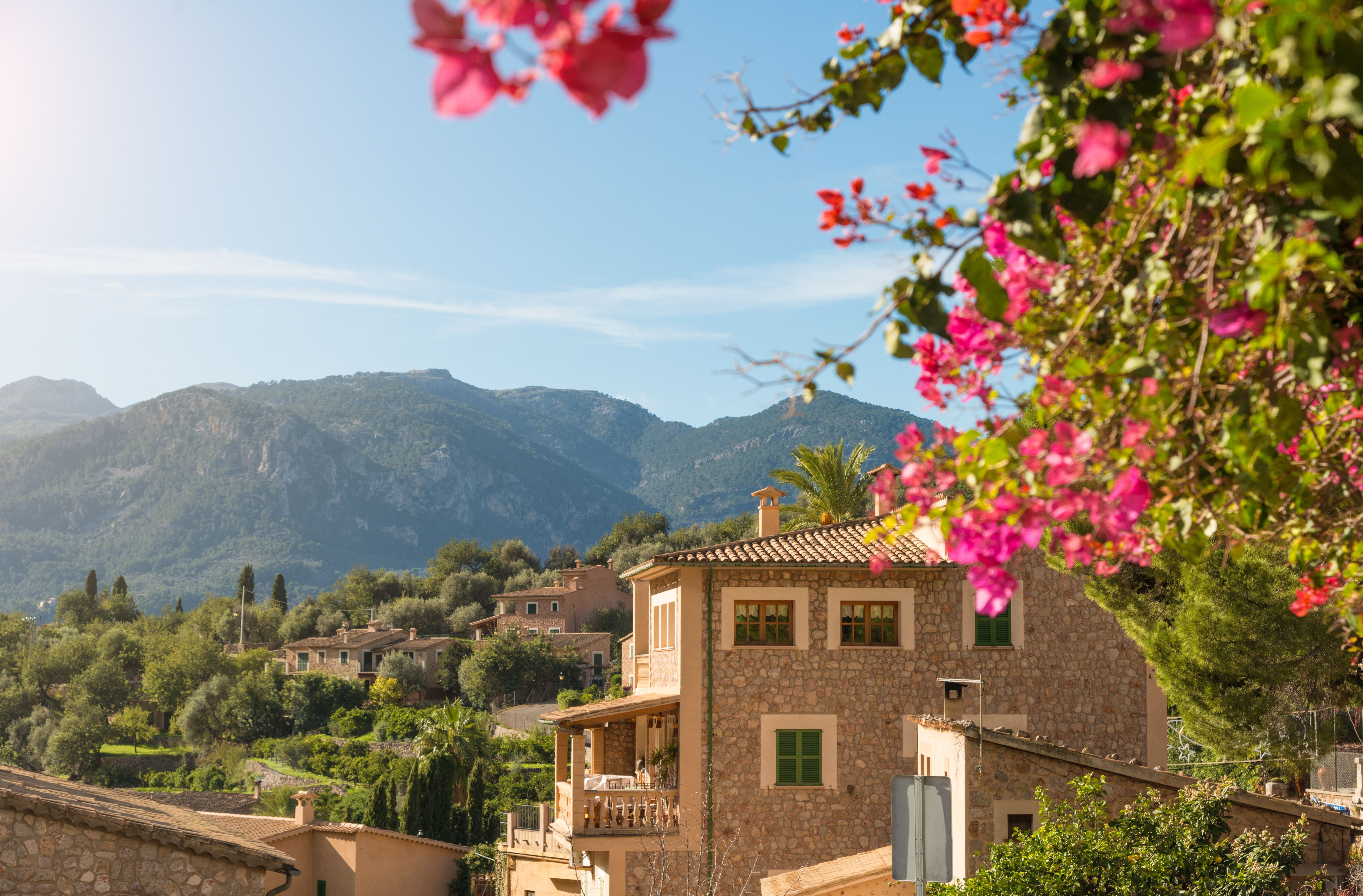 Steinhaus und Blumen im historischen Dorf Fornalutx auf Mallorca, mit Bergen im Hintergrund.