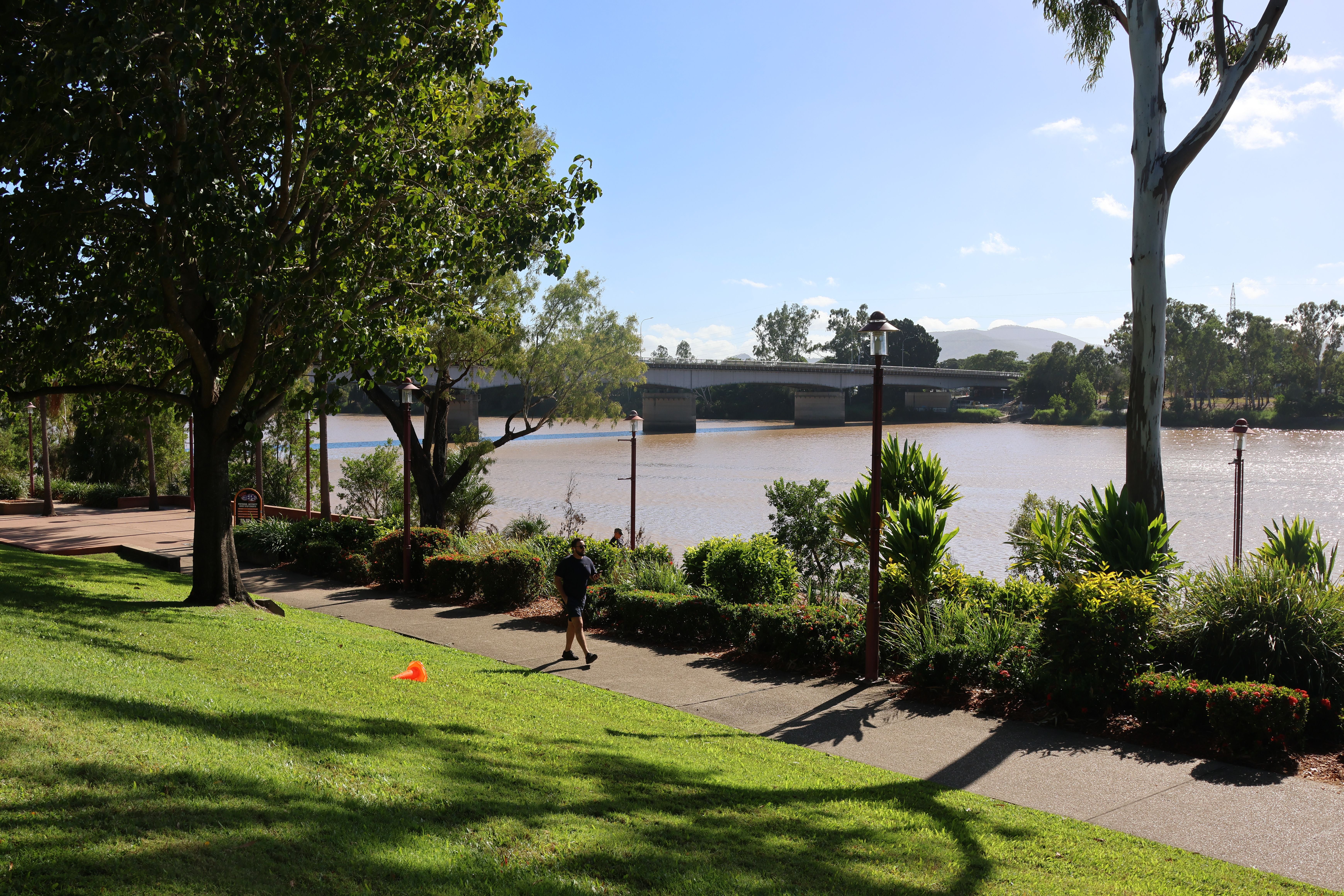 Person geht auf sonnigem Weg im Rockhampton Riverside Precinct am Fitzroy River entlang.
