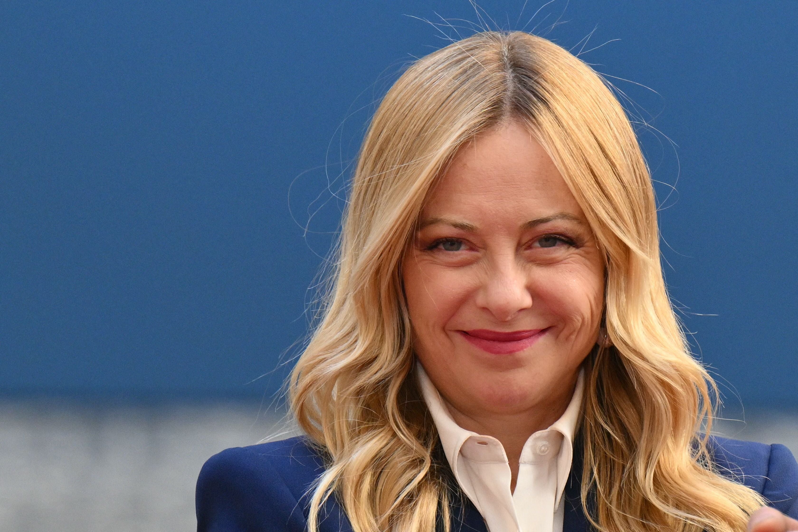 Frau mit blonden Haaren lächelt vor blauem Hintergrund in die Kamera.