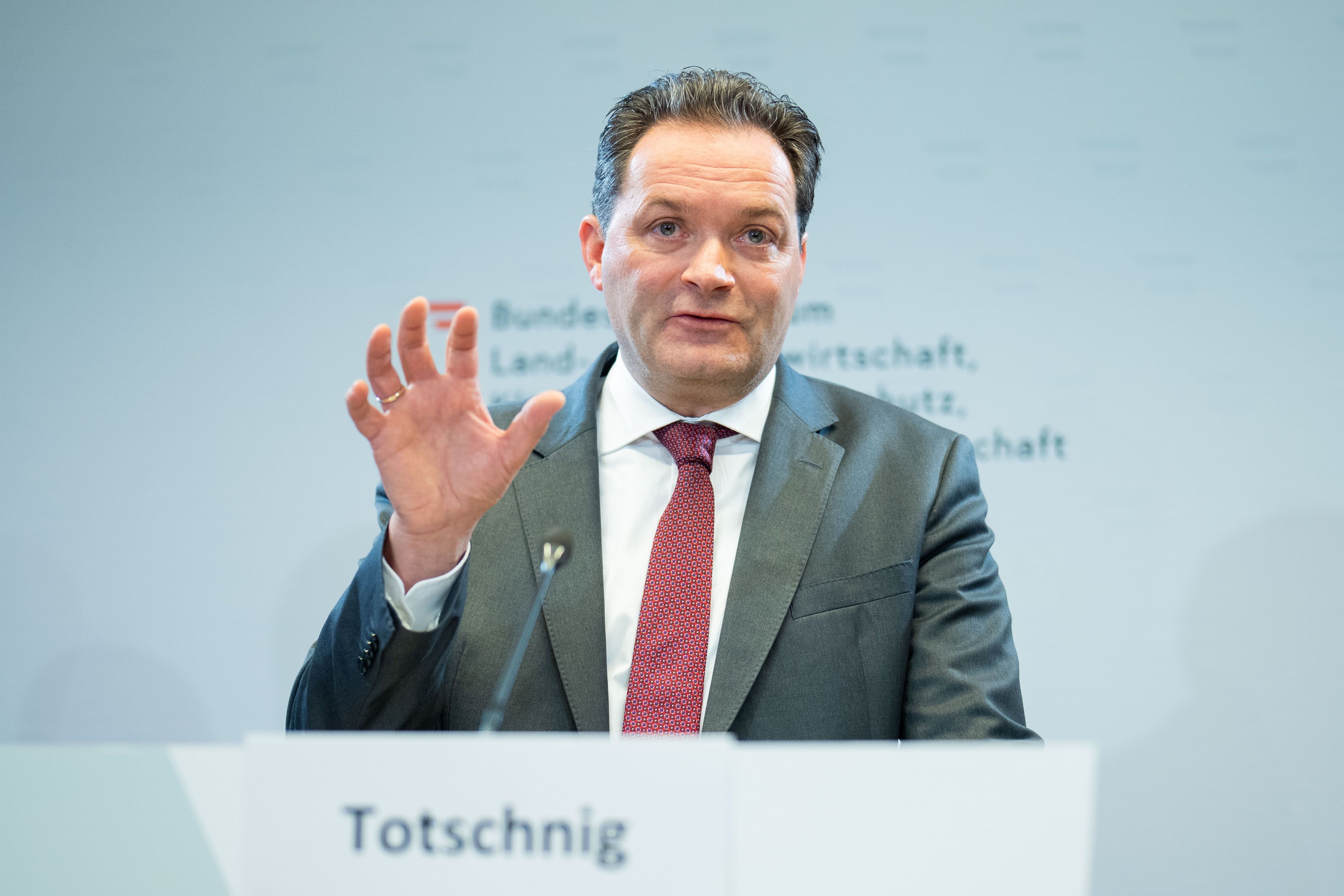 Ein Mann im Anzug spricht bei einer Pressekonferenz und hebt eine Hand gestikulierend an.