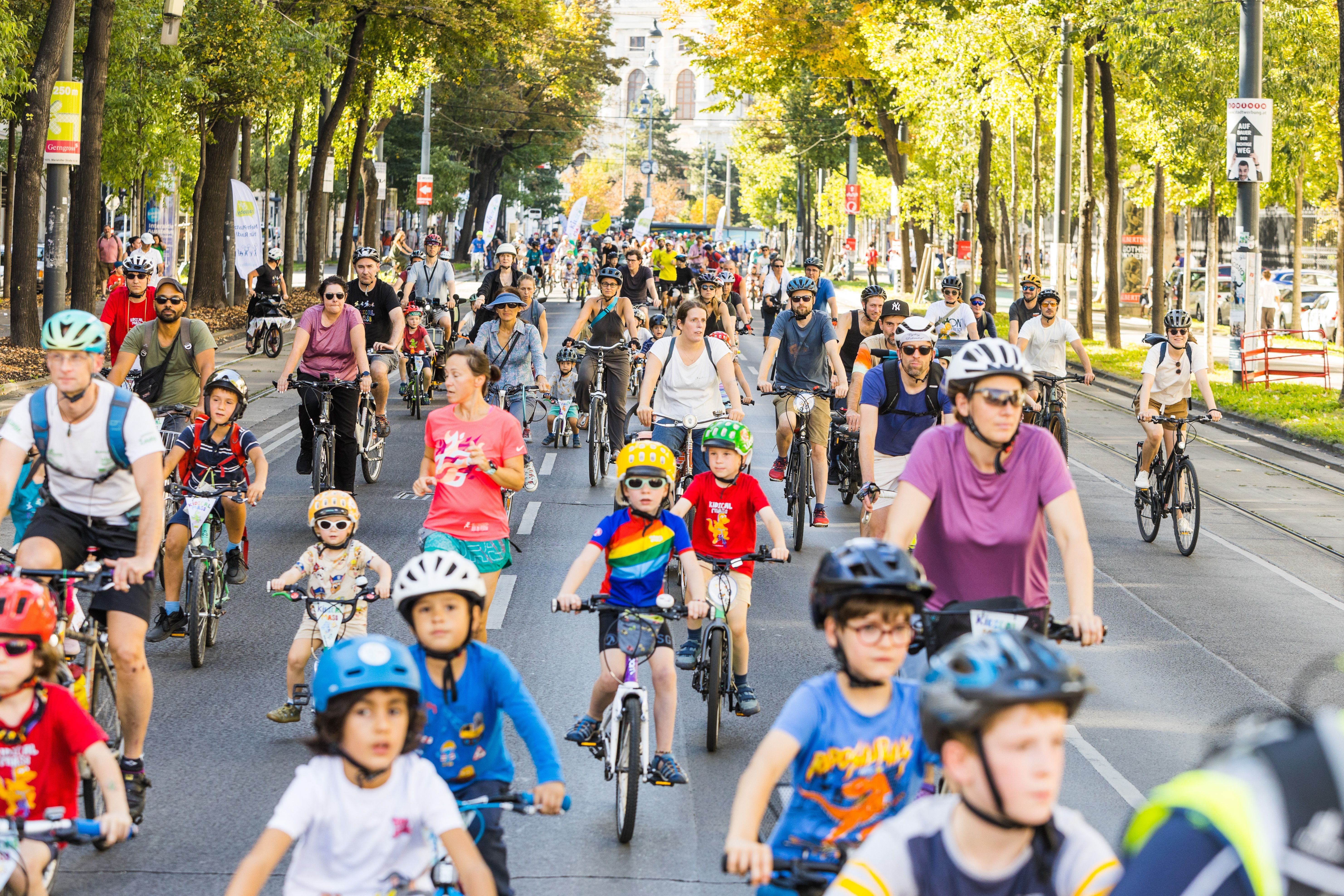 Viele Kinder und Erwachsene fahren bei einer Fahrraddemonstration durch eine von Bäumen gesäumte Straße.