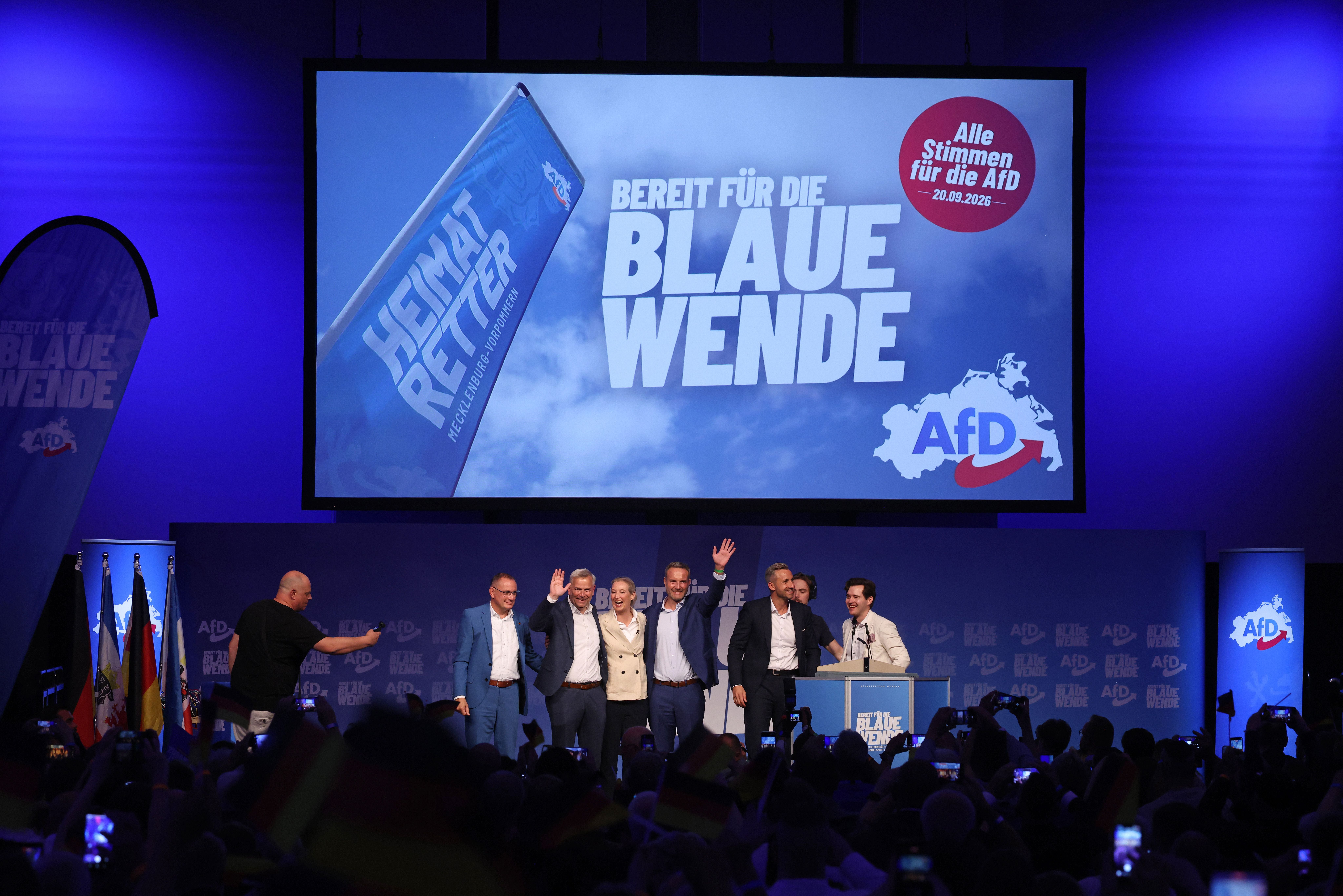 AfD-Politiker stehen auf einer Bühne bei einer Wahlkampfveranstaltung vor großem Wahlplakat.
