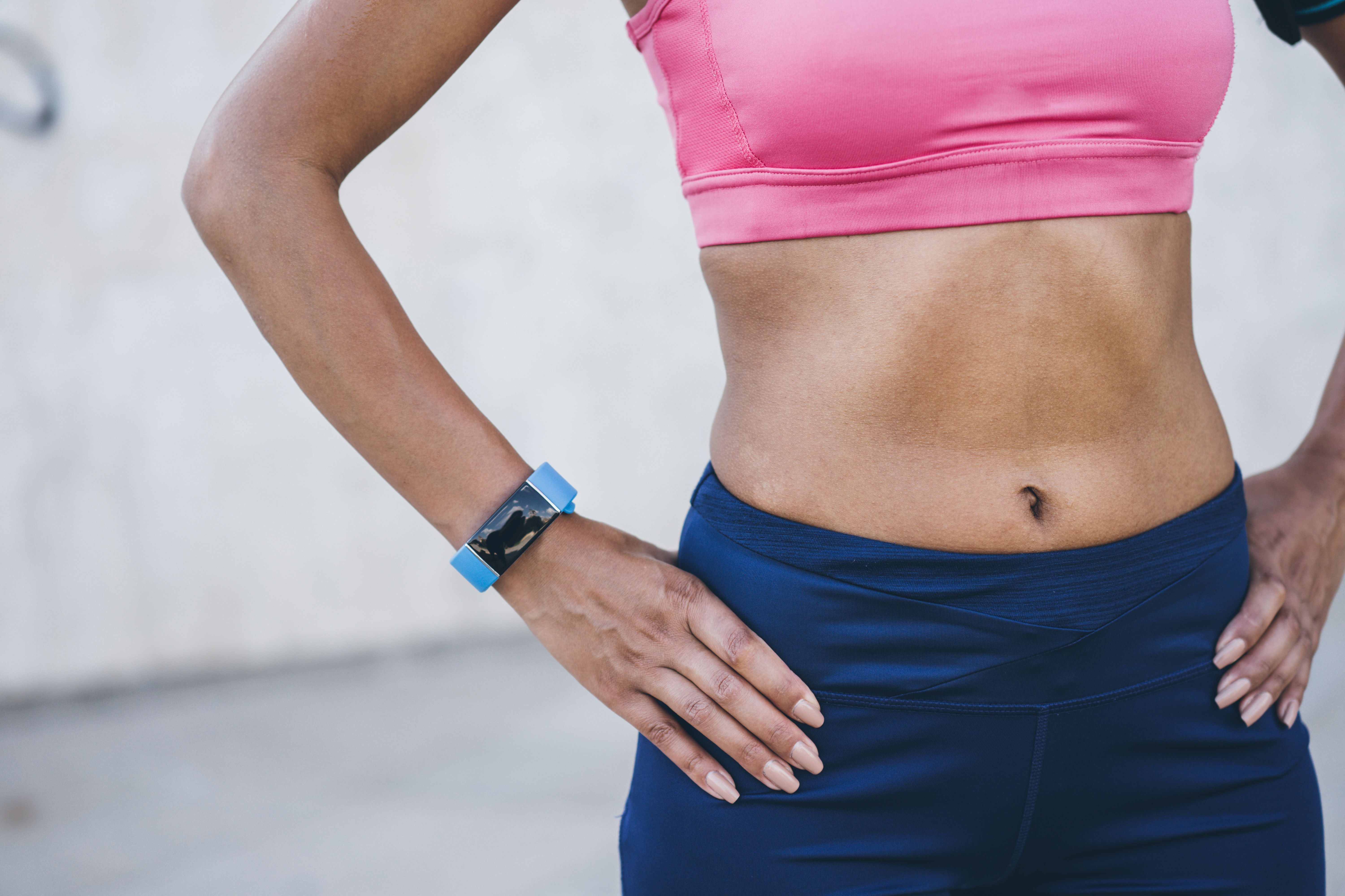 Sportlerin mit Händen in die Hüften gestemmt, trägt Sportkleidung und eine Smartwatch.