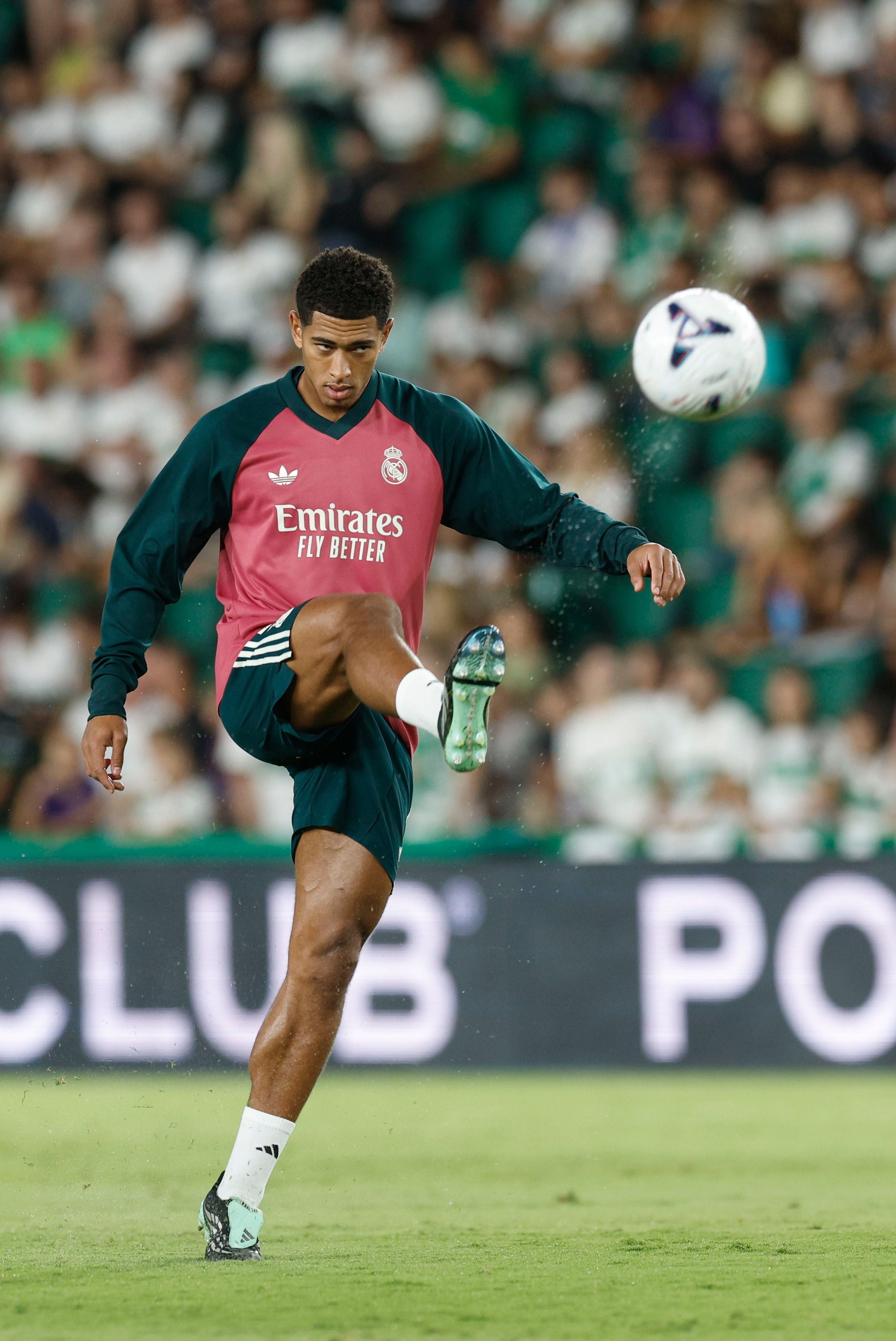 Jude Bellingham im rosa-dunkelgrünen Aufwärmtrikot von Real Madrid stoppt einen fliegenden Fußball mit hohem Bein auf dem Trainingsplatz.
