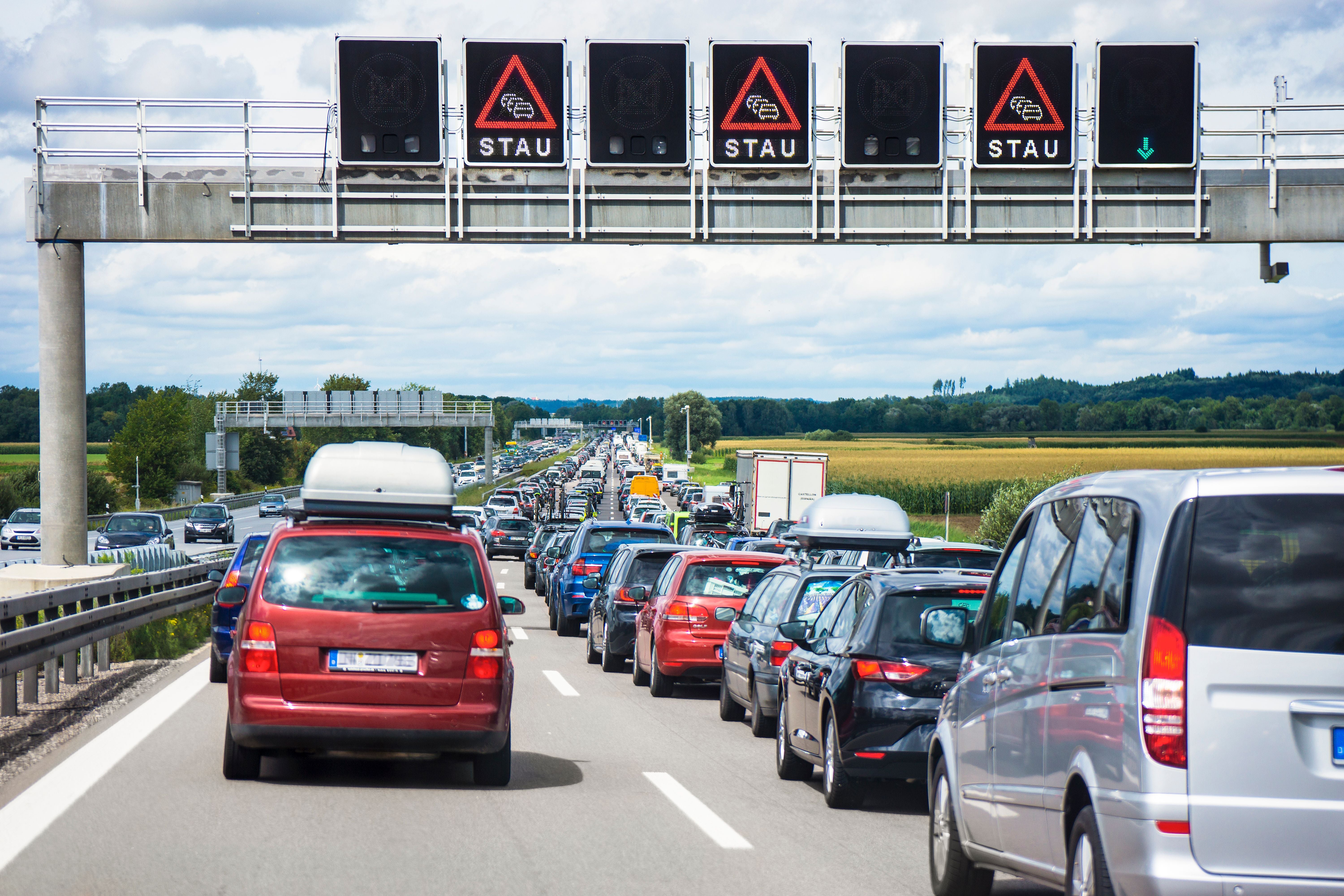 Langer Stau mit vielen Autos auf einer Autobahn unter einer Anzeige mit Stauwarnung.