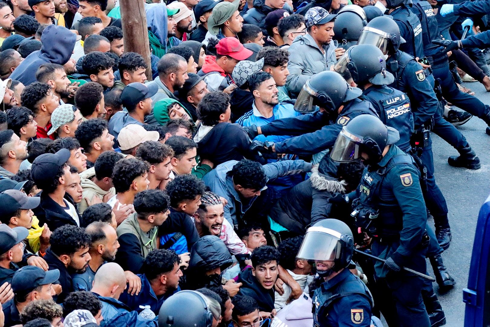 Viele Migranten stehen dicht gedrängt, während Polizisten in Schutzkleidung sie zurückhalten.