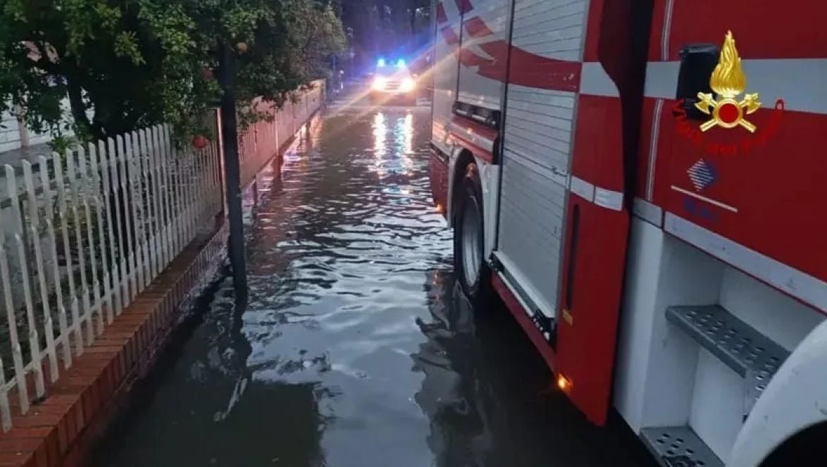 Feuerwehrauto steht auf einer überfluteten Straße in Italien, Blaulicht im Hintergrund.