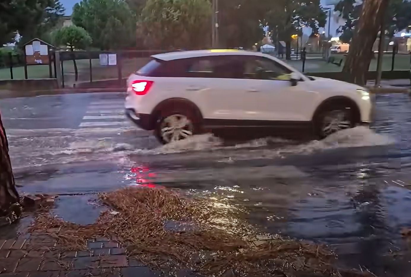 Ein weißes Auto fährt durch eine überflutete Straße bei starkem Regen in Jesolo.