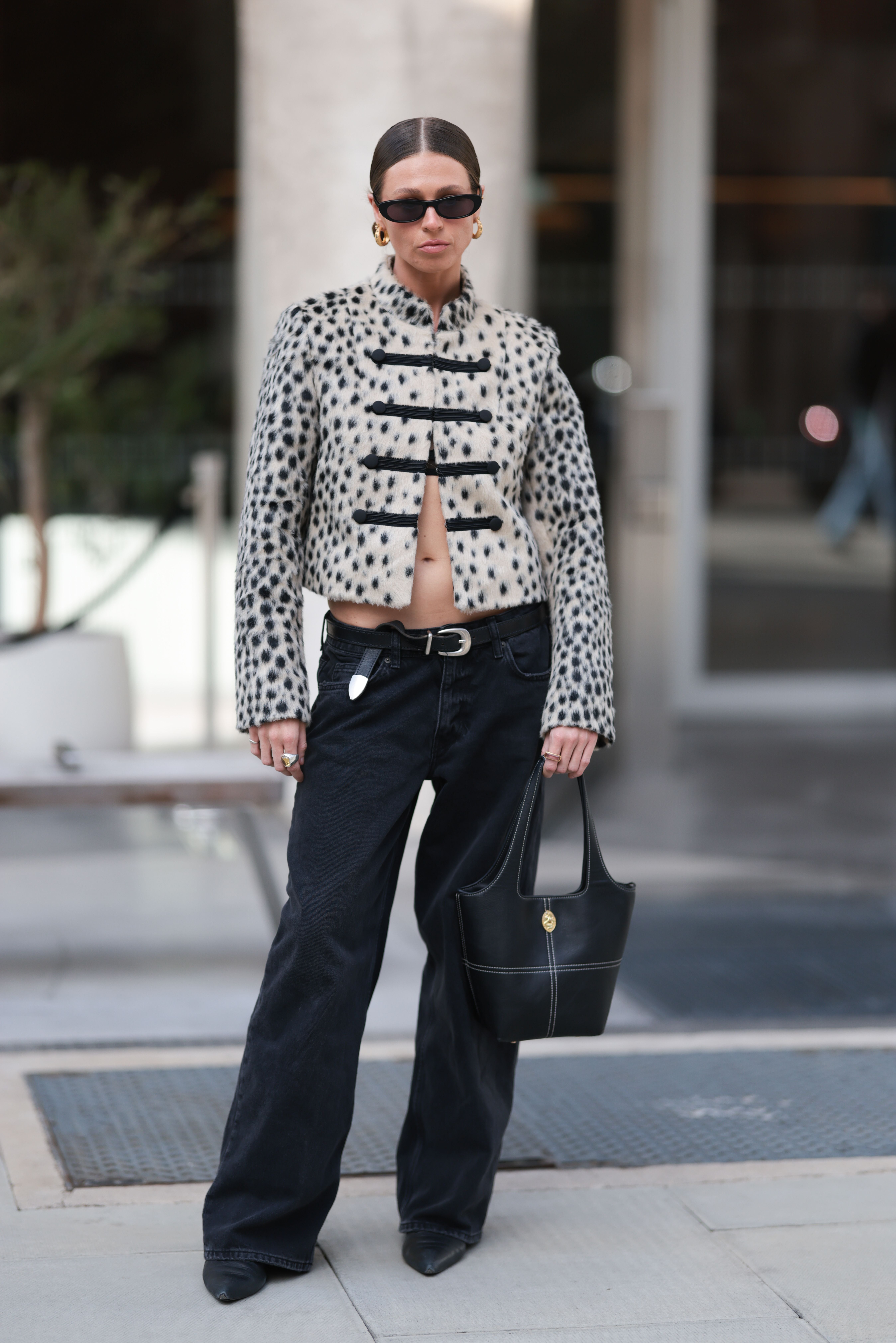 Frau mit Leopardenprint-Jacke, schwarzer weiter Hose, schwarzer Tasche und Sonnenbrille.