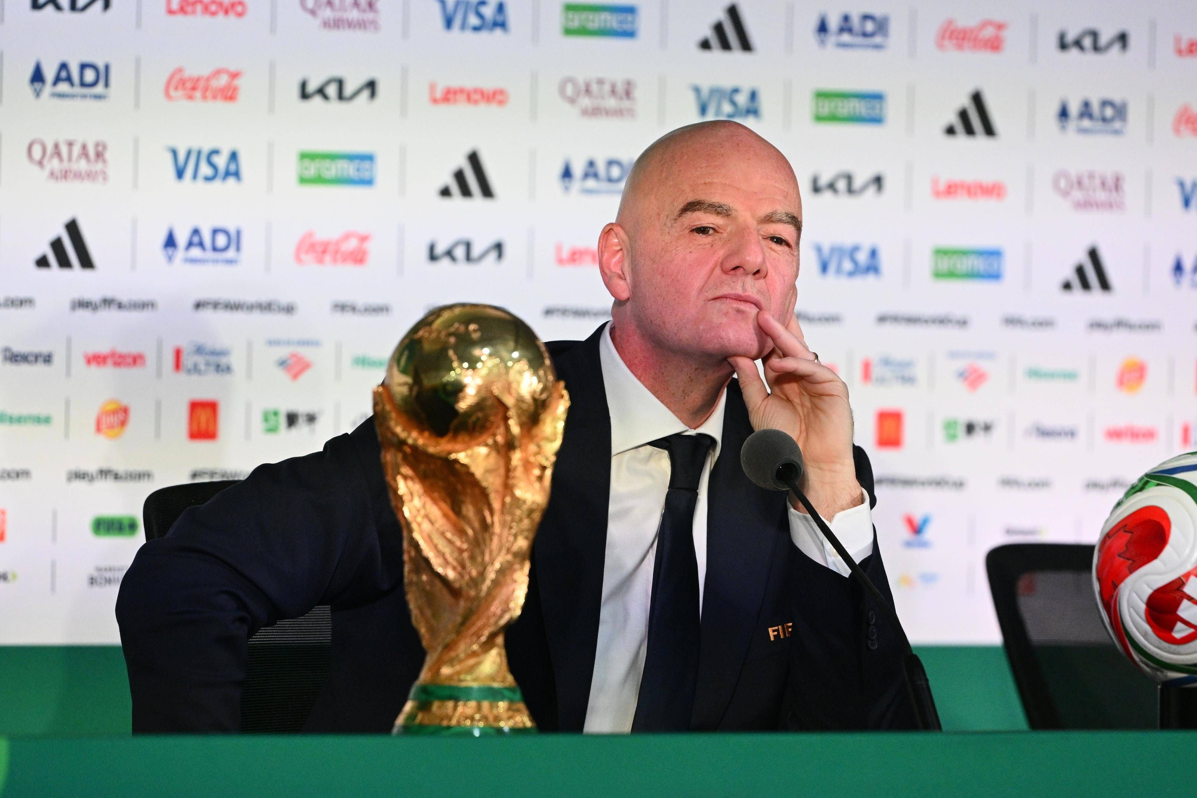 Gianni Infantino im Anzug sitzt nachdenklich mit abgestütztem Kinn hinter dem FIFA-WM-Pokal bei einer Pressekonferenz.