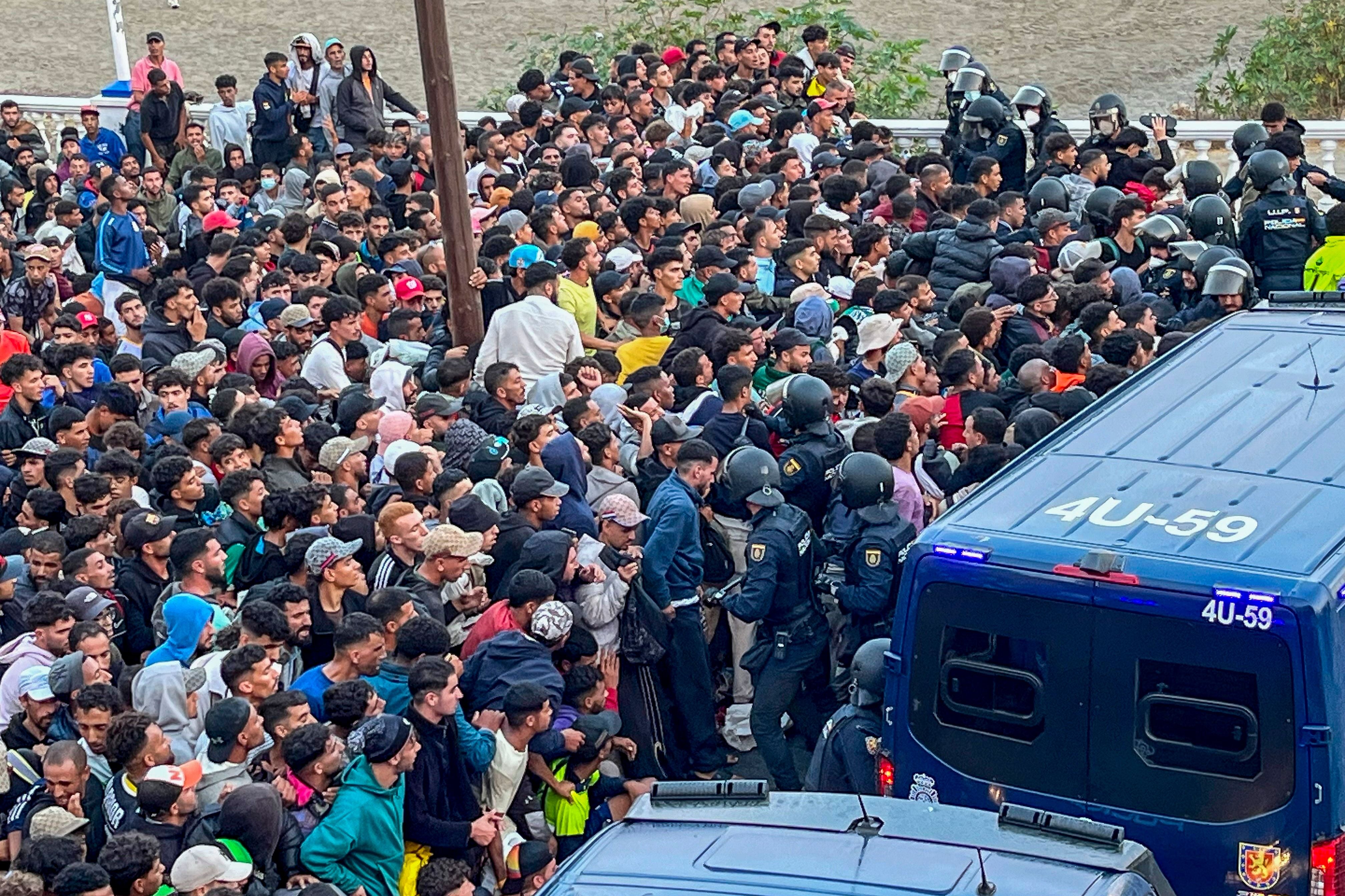 Viele Migranten stehen gedrängt an einem Strand, Polizeieinheiten und Einsatzwagen sind im Einsatz.