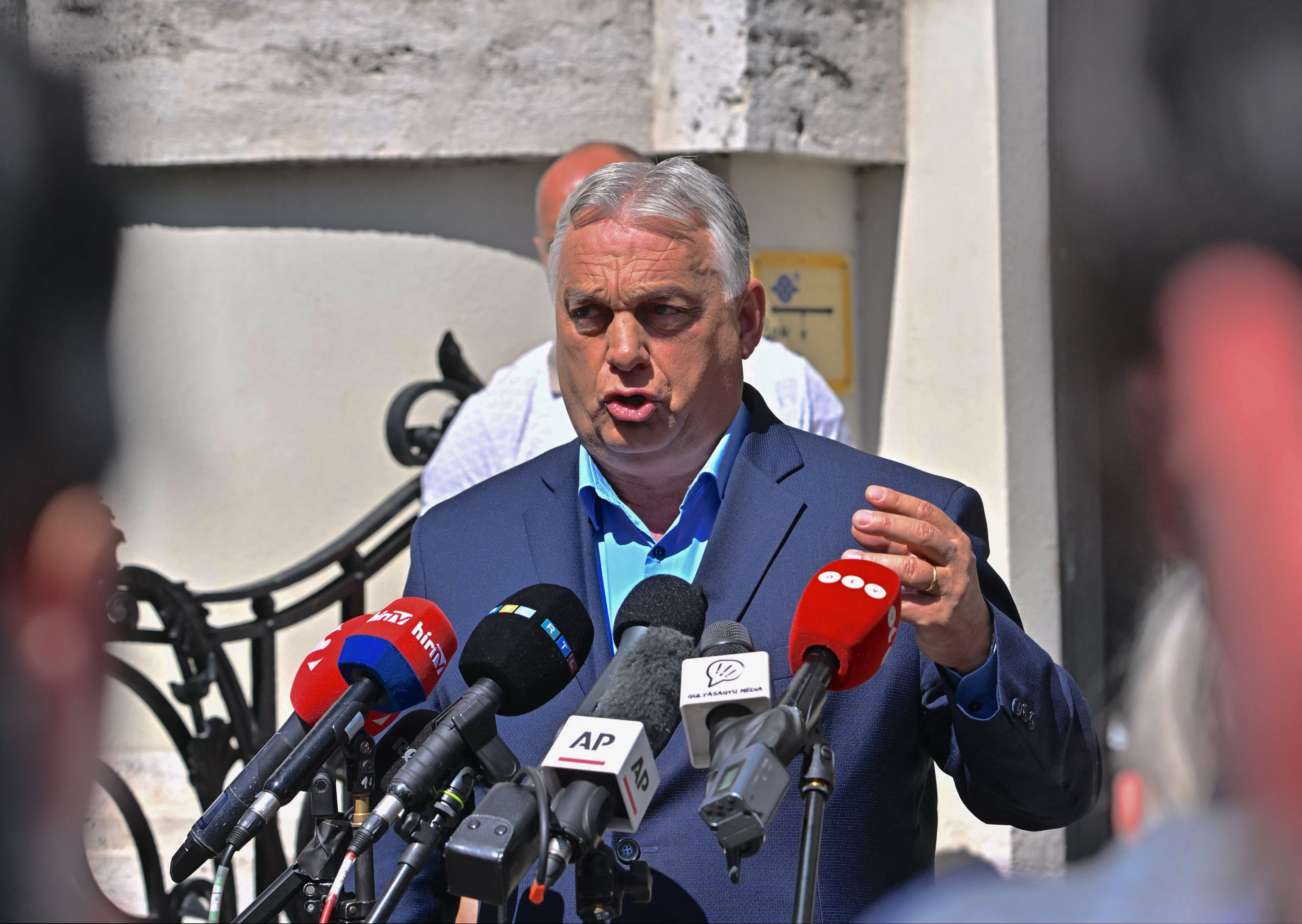Ein Mann im Anzug spricht bei einer Pressekonferenz vor mehreren Mikrofonen im Freien.