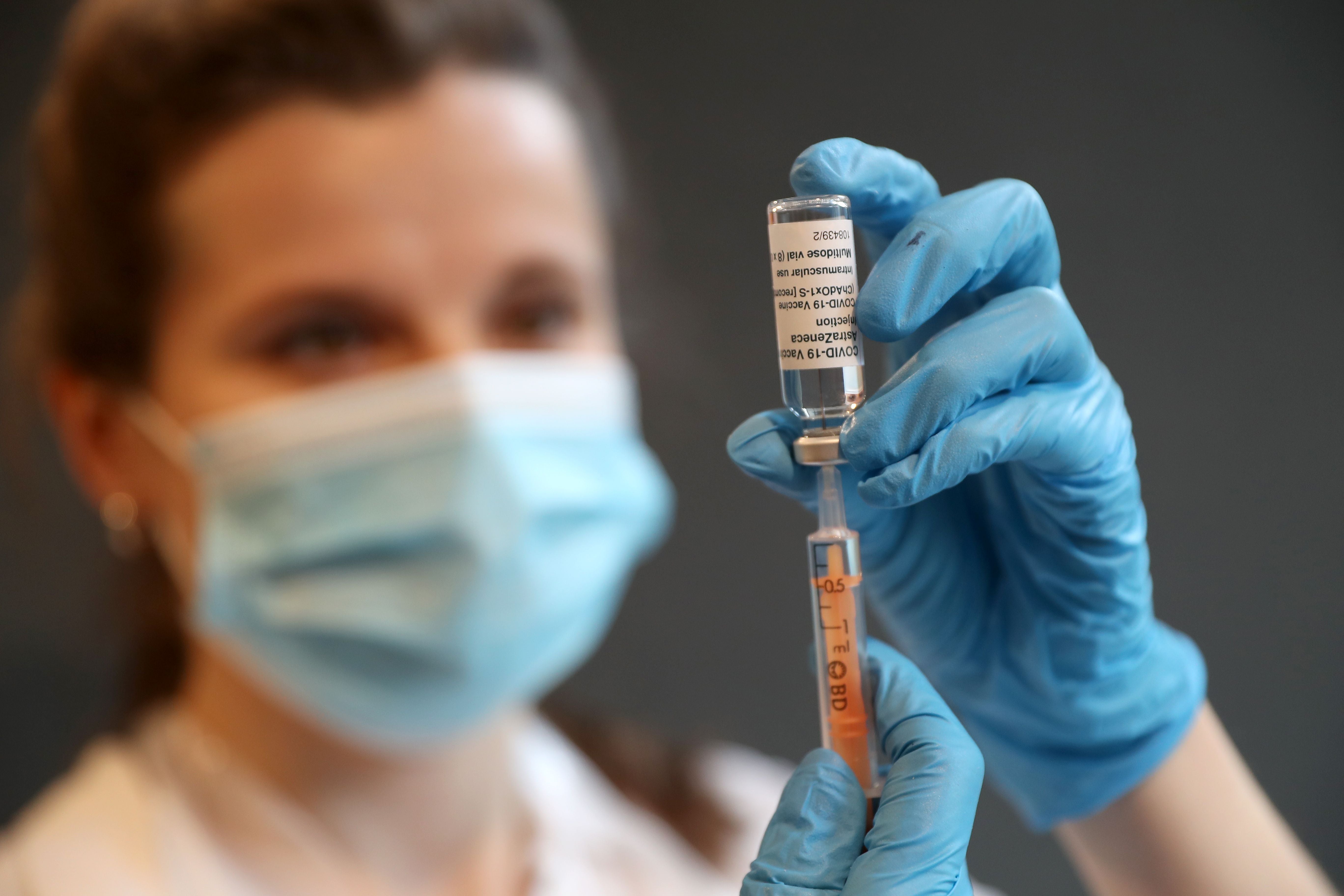 Eine Person mit Maske zieht eine Dosis AstraZeneca-Impfstoff in eine Spritze auf.