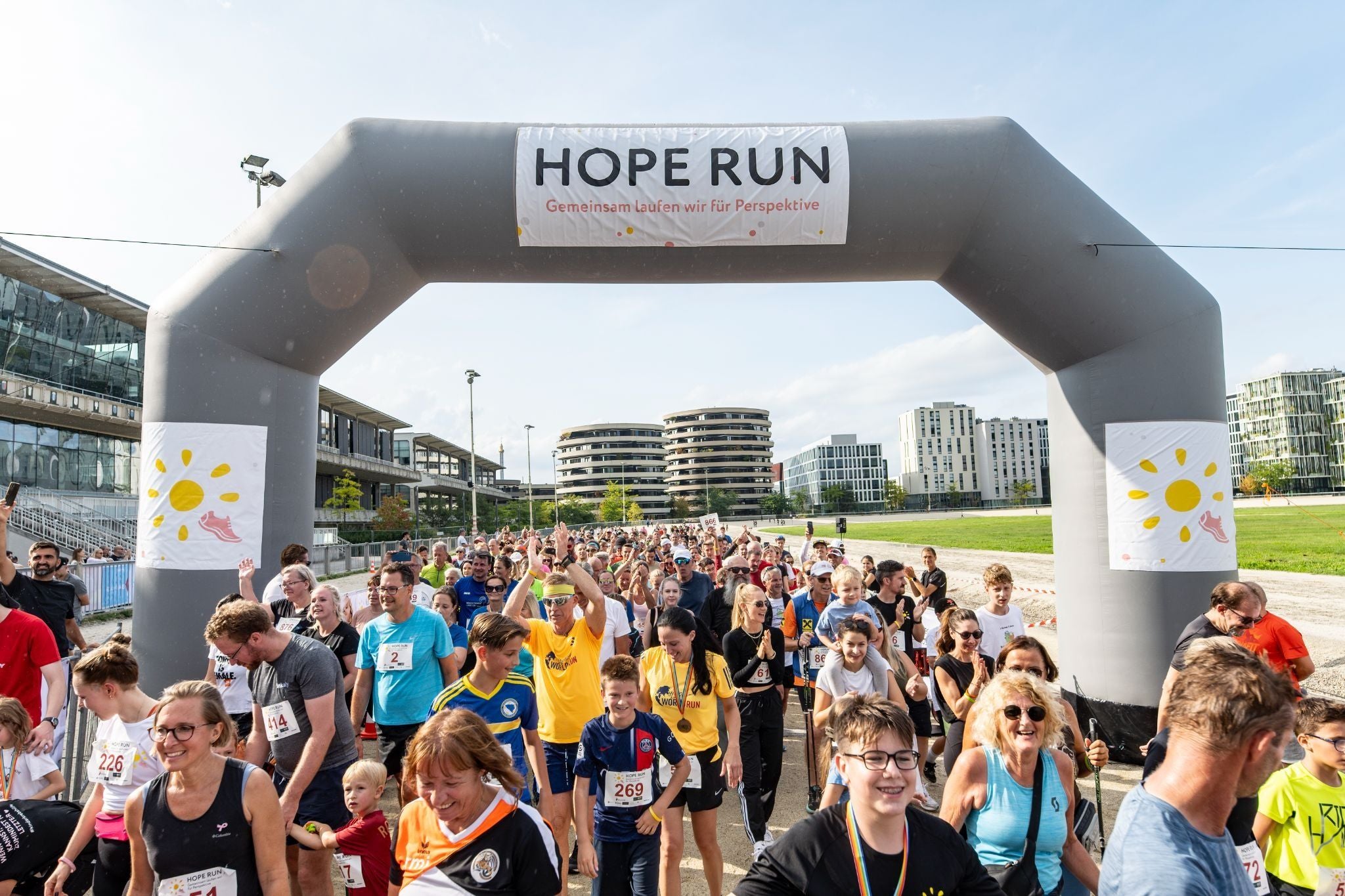 Viele Menschen laufen beim Hope Run in Wien unter einem großen Startbogen im Freien.