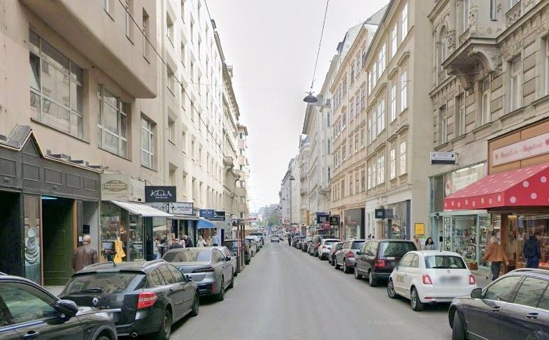 Belebte Straße mit parkenden Autos und Geschäften auf beiden Seiten in der Wollzeile, Wien.